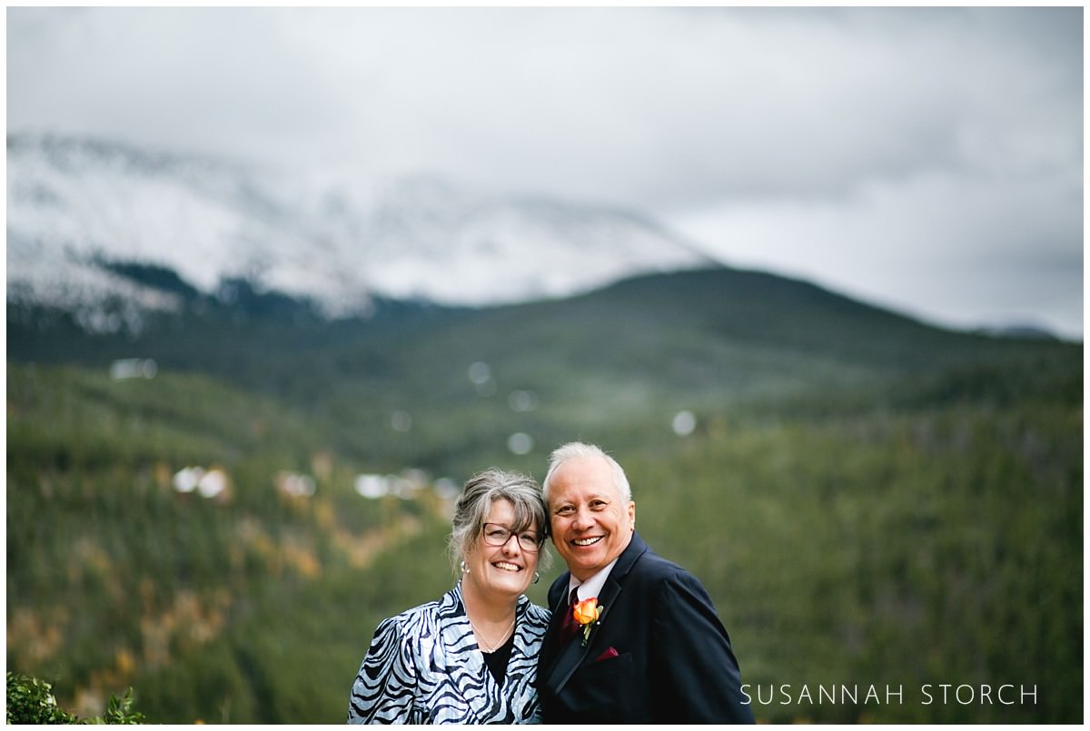 parents of the groom stand in front of snowy mountains