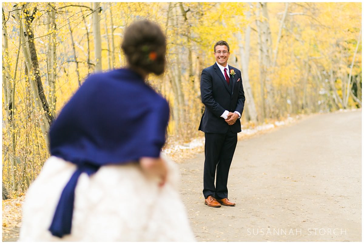 a groom looks towards his bride while standing in front of yellow aspen trees