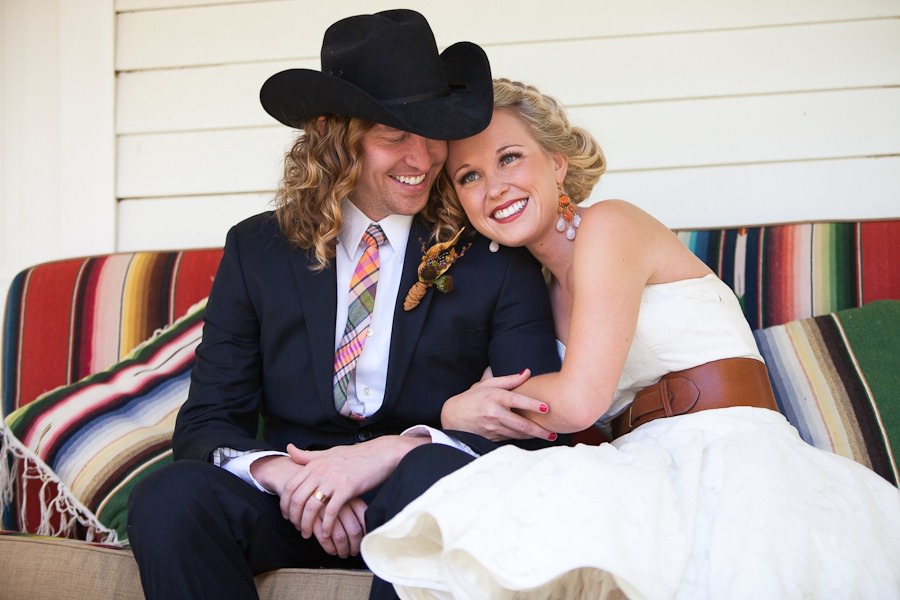 a cowboy and his bride sit on a colorful couch on a porch
