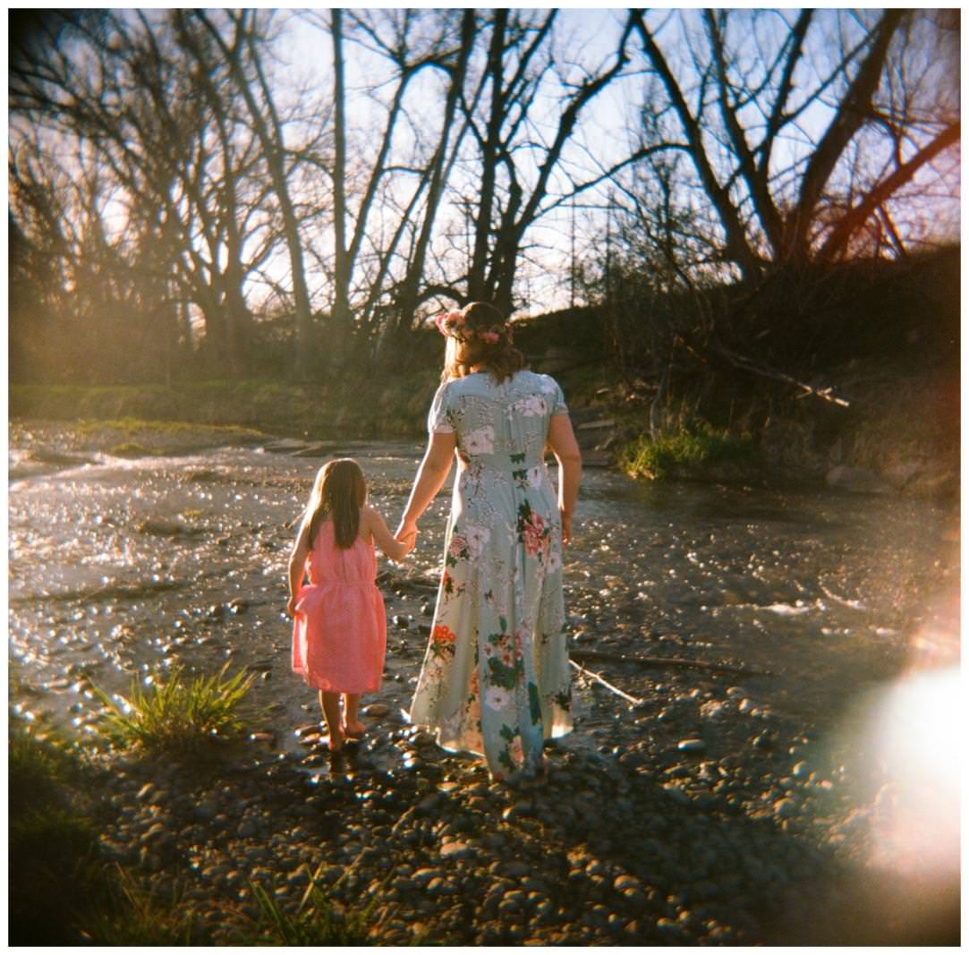 A mom and daughter hold hands and walk in the woods