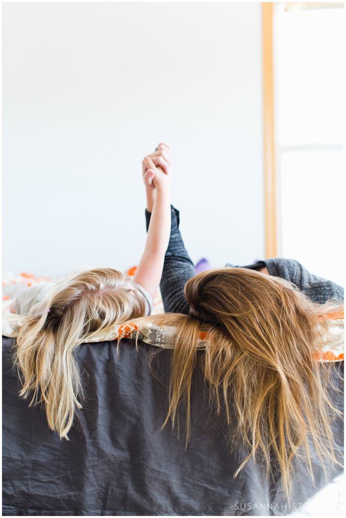 a mom and daughter hold hands as their hair spills over a bed