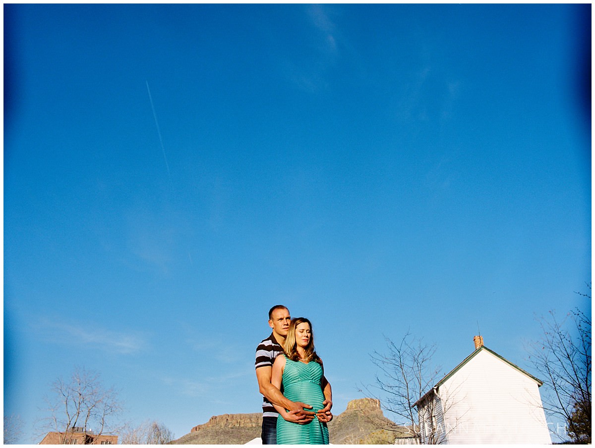 a pregnant couple embrace under blue skies