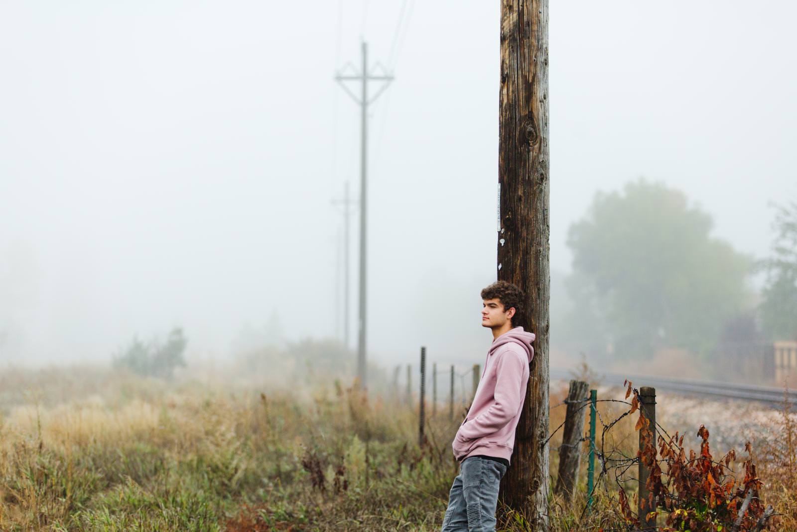 colorado senior photography of teen leaning against a pole on a misty morning