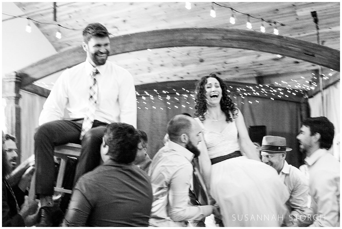 black and white of bride and groom in chairs during the hora
