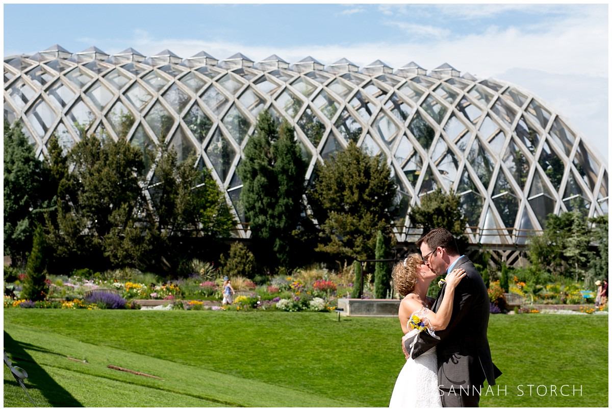a wedding couple kiss in front of a building at the Denver Botanic Gardens