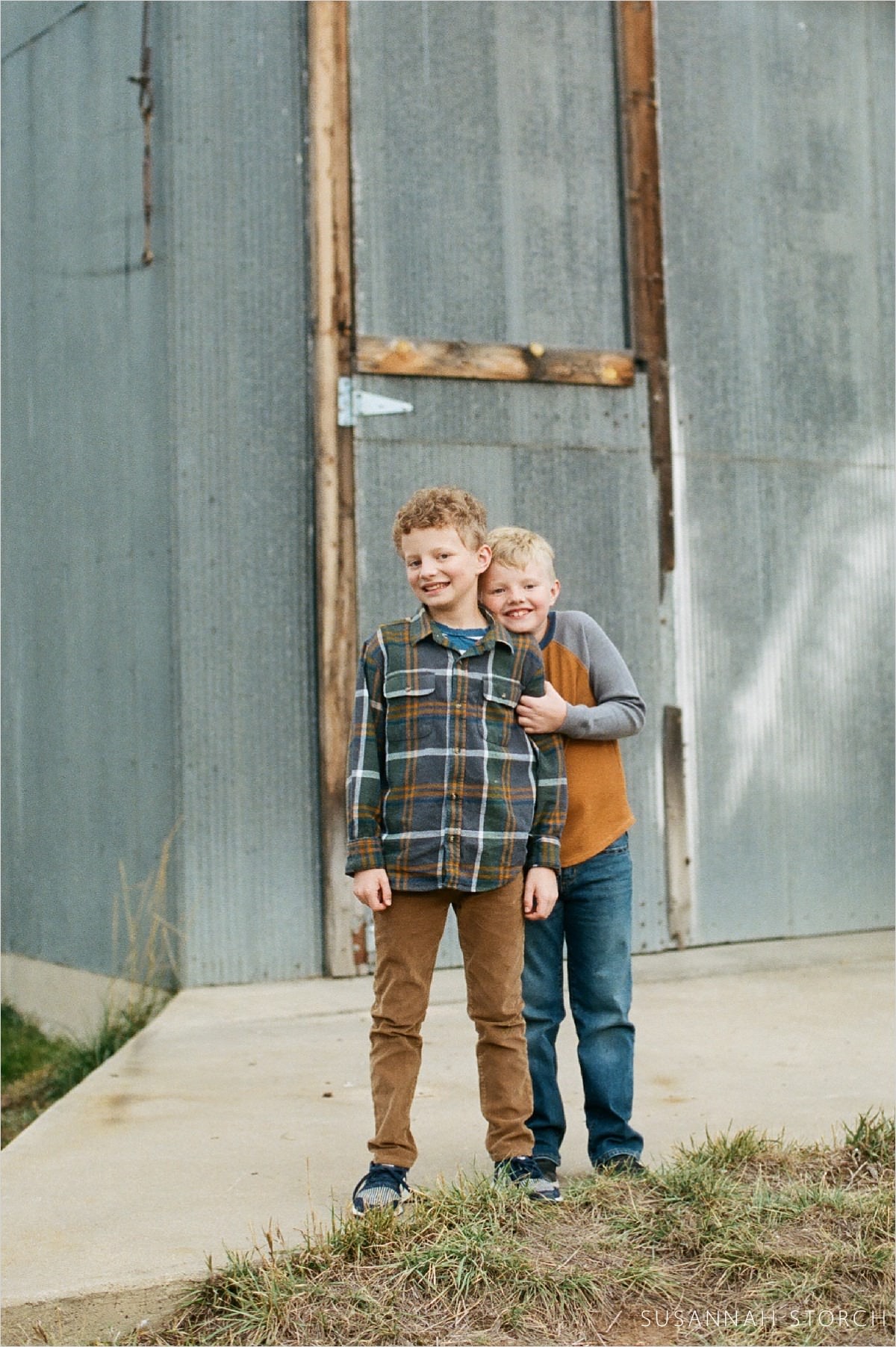 brothers hug in front of old industrial/farm building