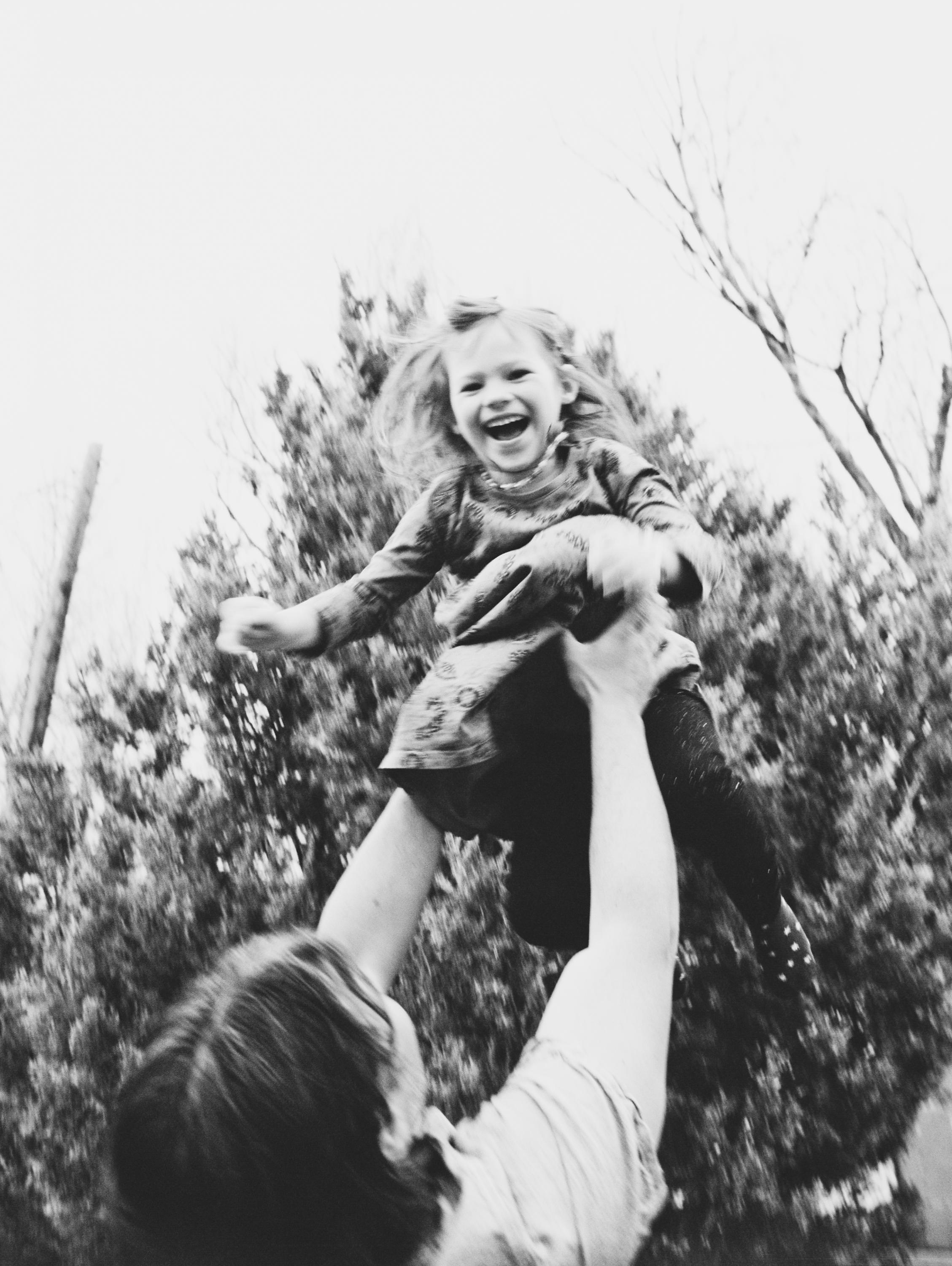 A black and white image of a dad throwing his girl into the air