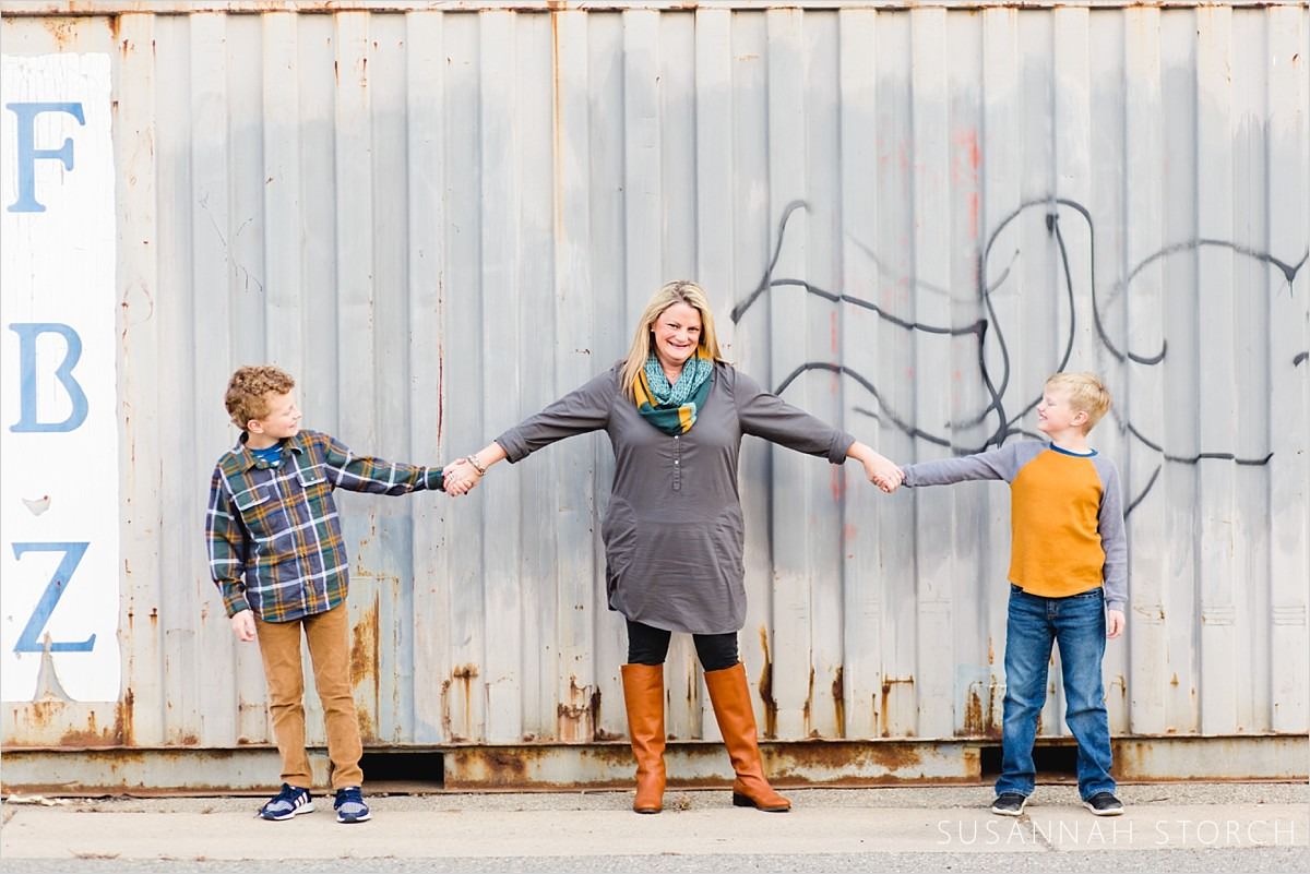 a mom holds hands of her sons in front of a shipping container