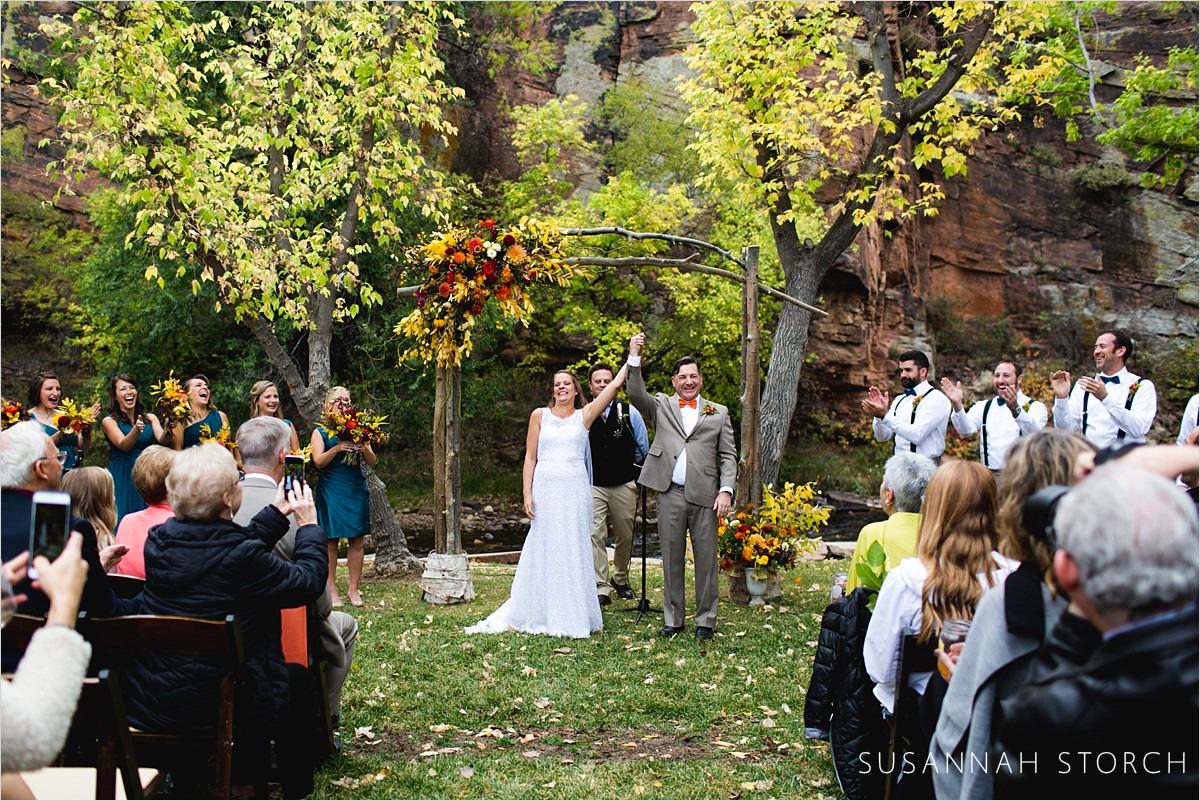 bride and groom raise their arms into the air after their outdoor fall wedding ceremony