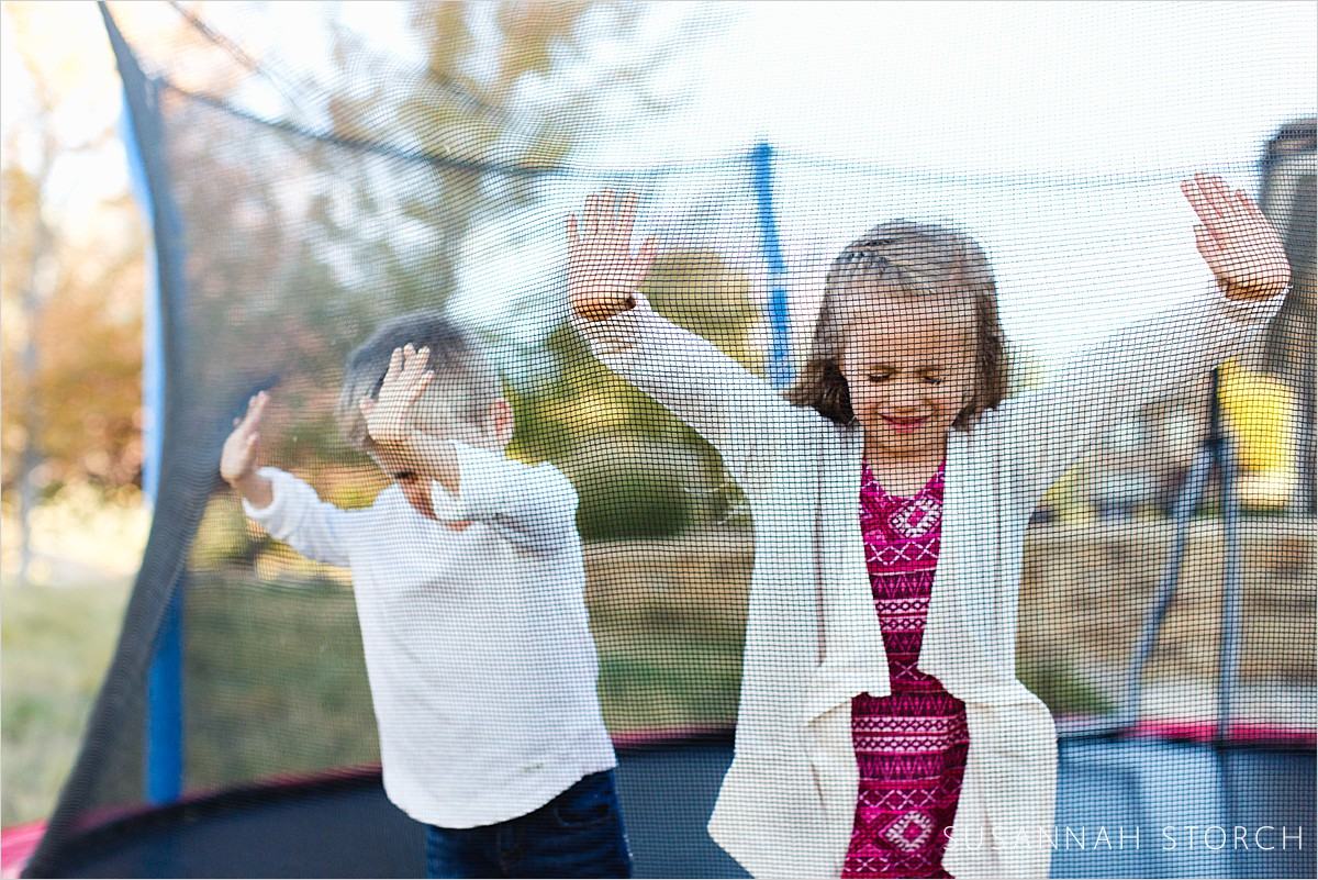 siblings push on the netting of a trampoline