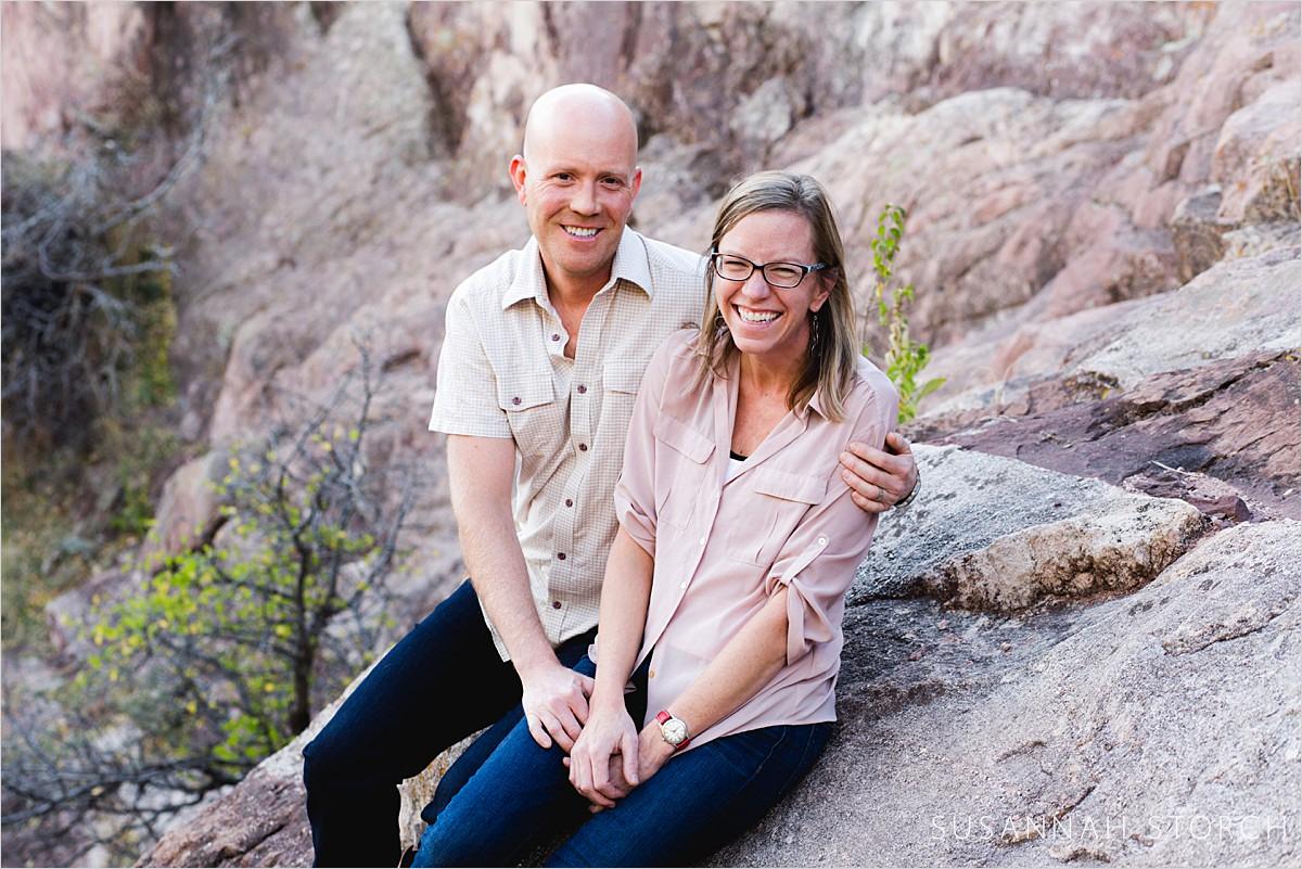 husband and wife laugh while sitting on rocks at a park in boulder, colorado