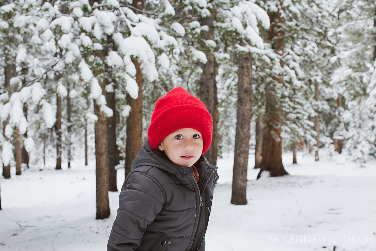 son in red hat stands in snowy woods