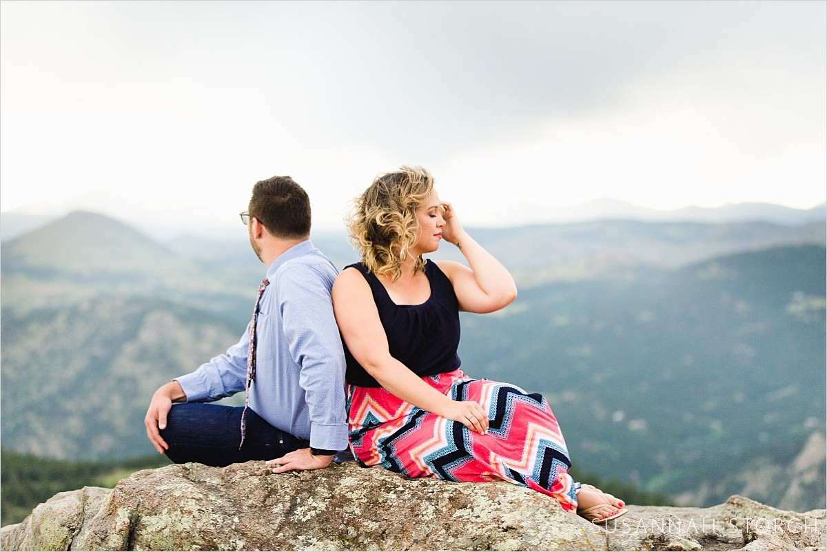 a couple sit on a rock in front of mountains