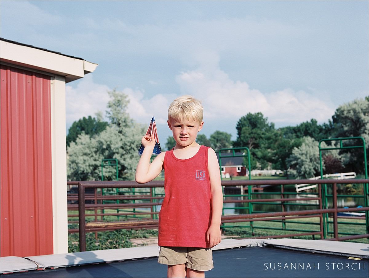 boy in red tank stands on trampoline and holds a paper airplane