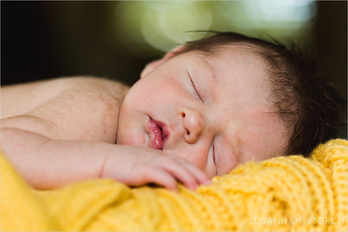 cute newborn baby with eyes closed lying on yellow blanket