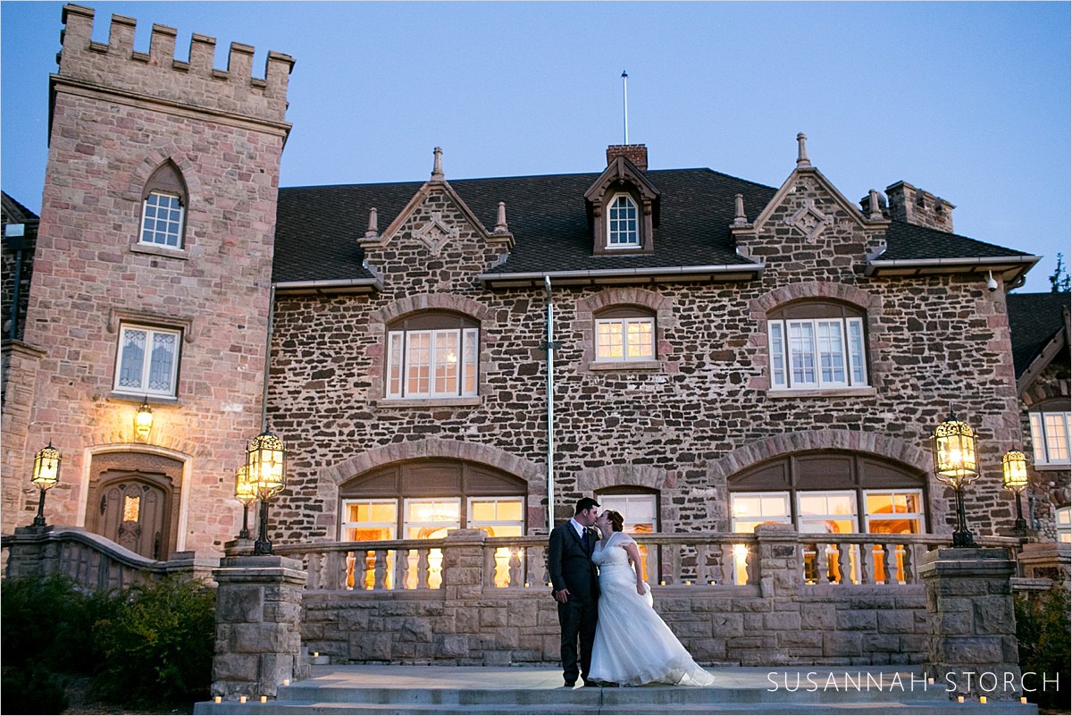 a couple kiss at dusk in front of a stone mansion