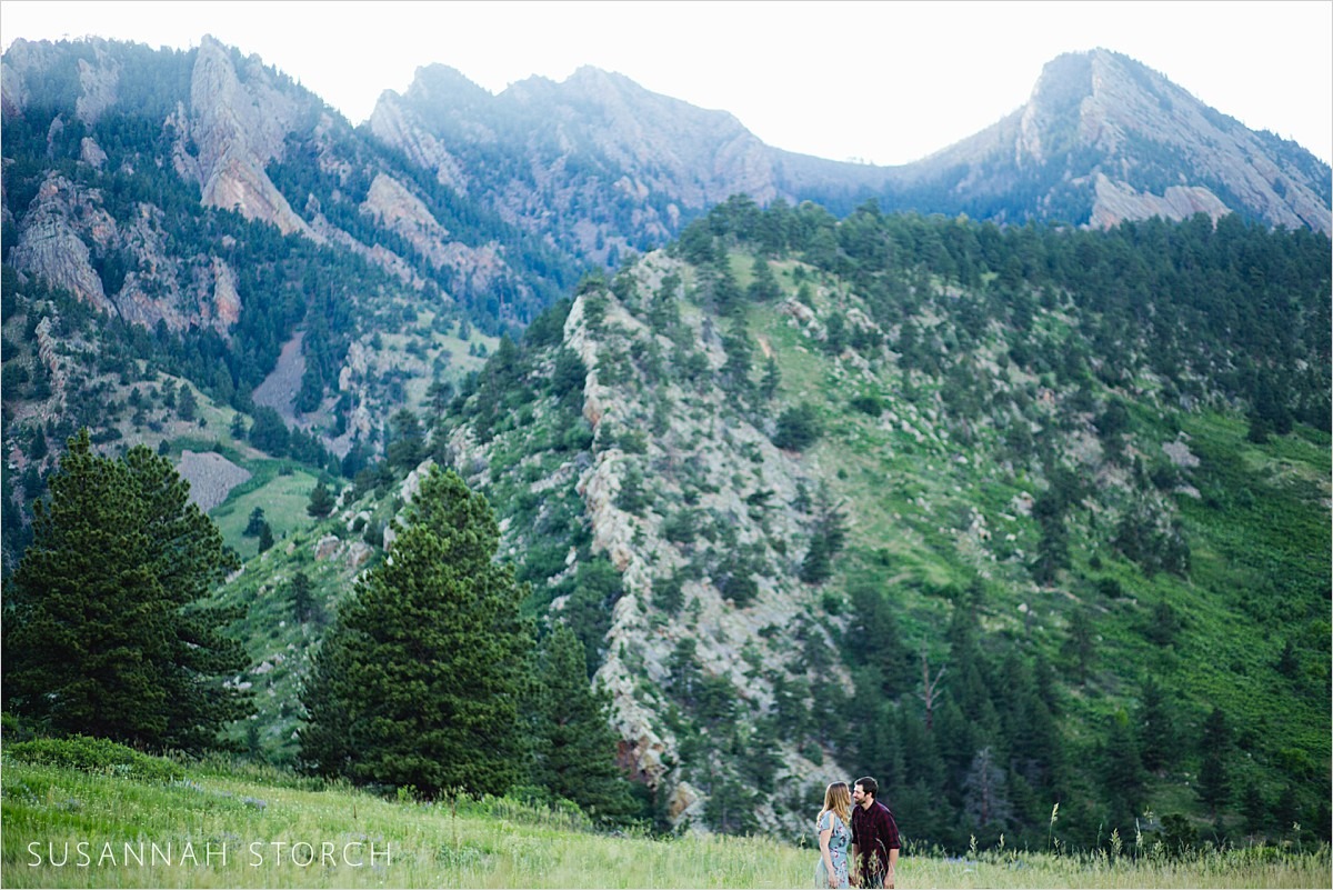 a couple stand in front of a green mountain in boulder, co