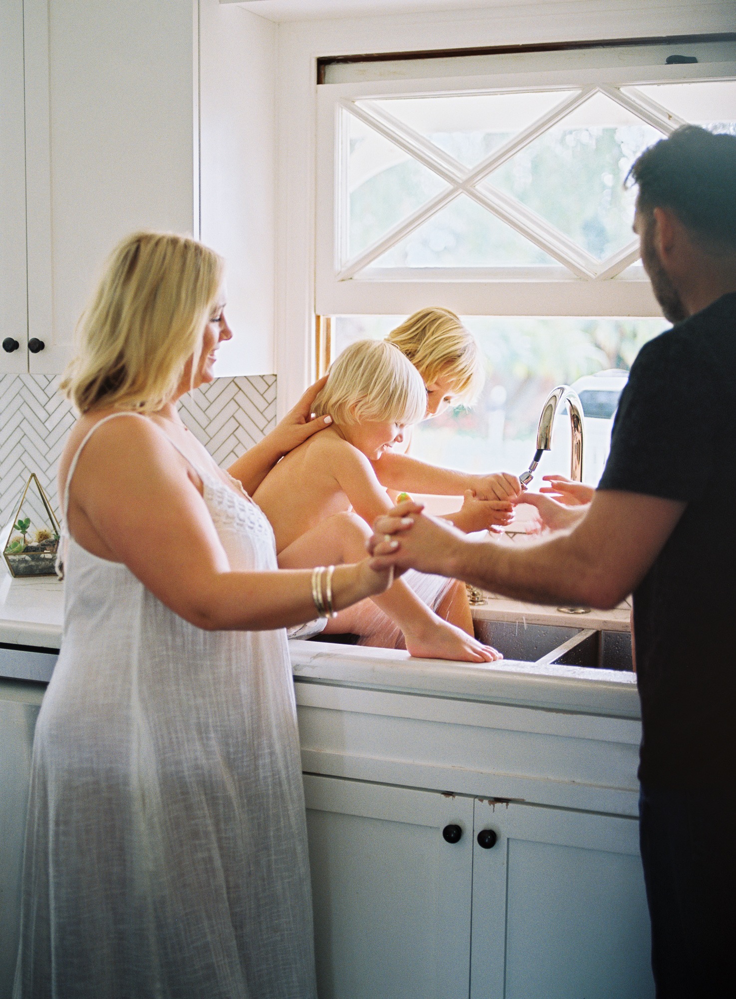 a family plays in the kitchen sink while being photographed by a professional family photographer