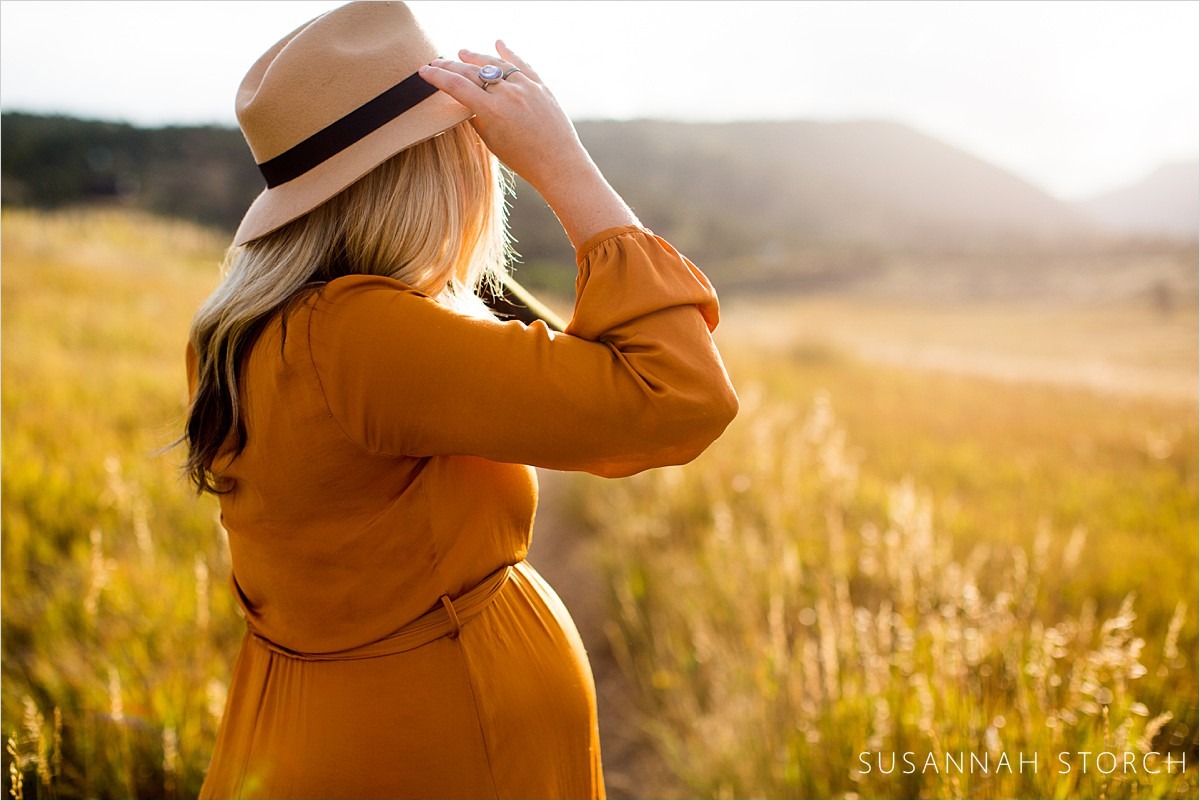 pregnant mama in orange dress adjusts hat at sunset