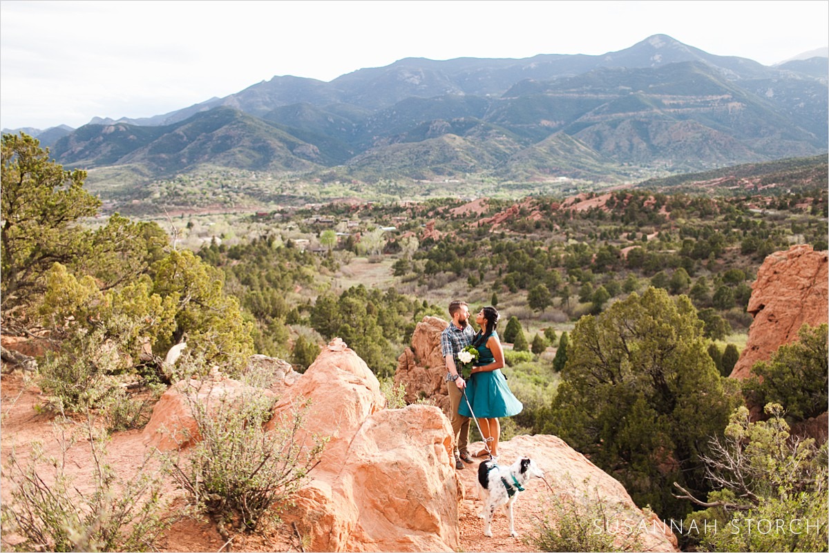 a couple stand on a rock in front of mountains in garden of the gods