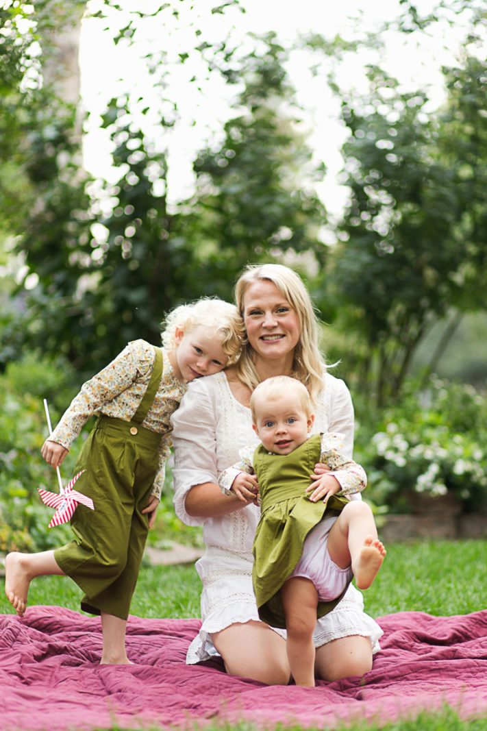 mom and daughters sit in front of green bushes during family photo session at Thompson Park in Longmont, Colorado