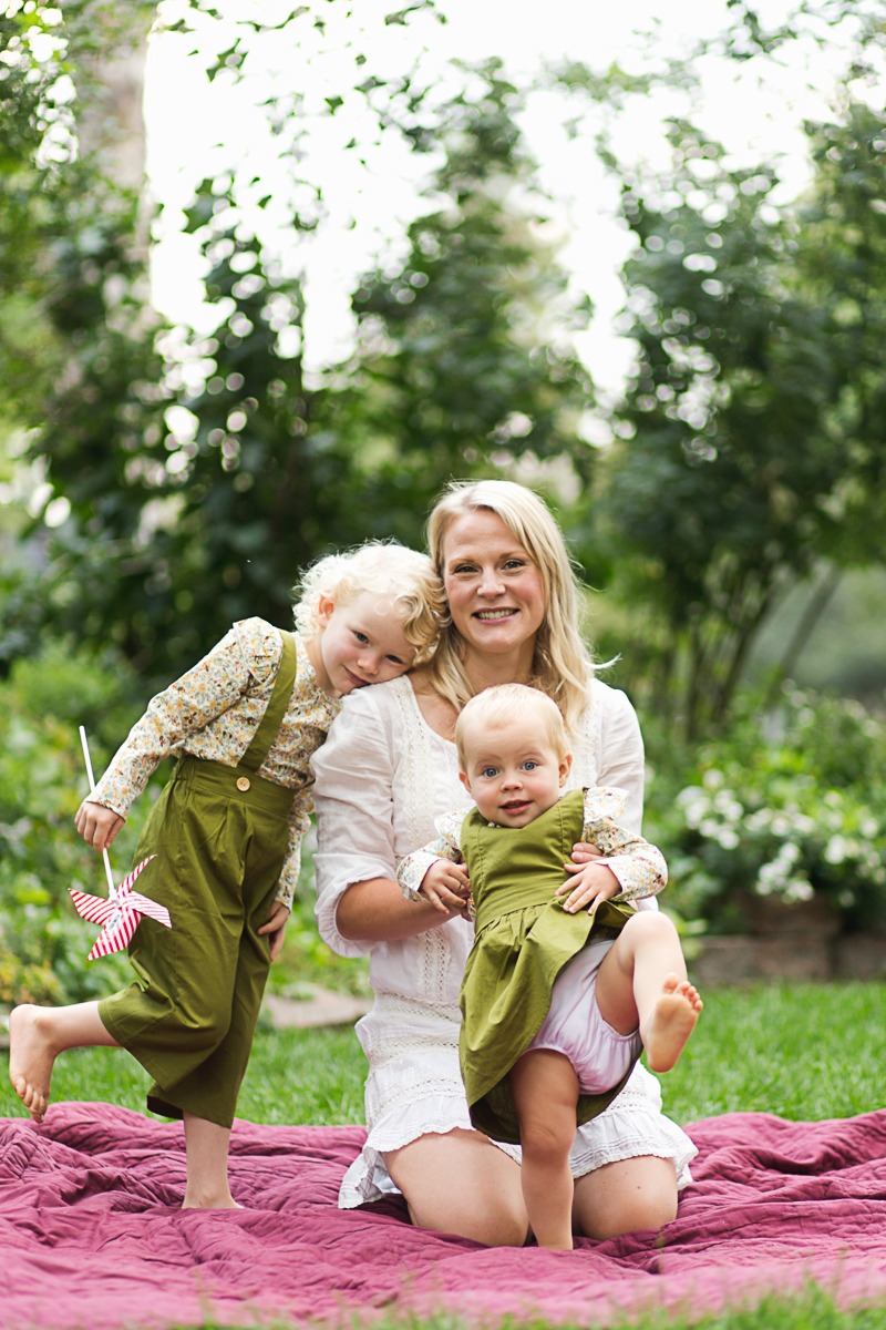 mom and daughters sit in front of green bushes during family photo session at Thompson Park in Longmont, Colorado