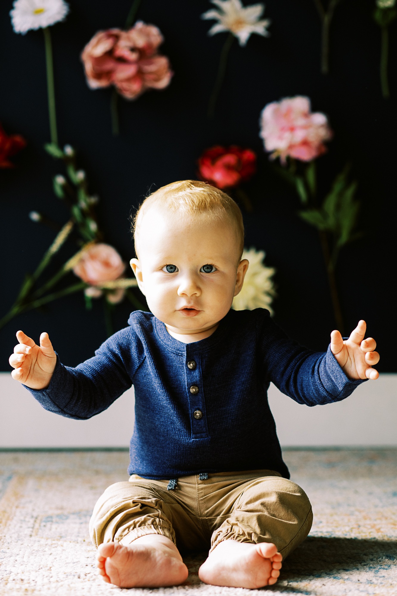 cute baby boy sits in front of wall with flowers