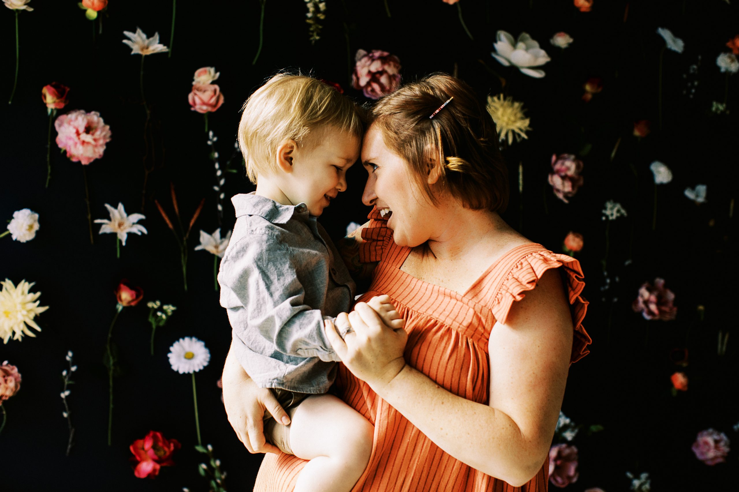 mom looks at toddler boy in front of floral wall