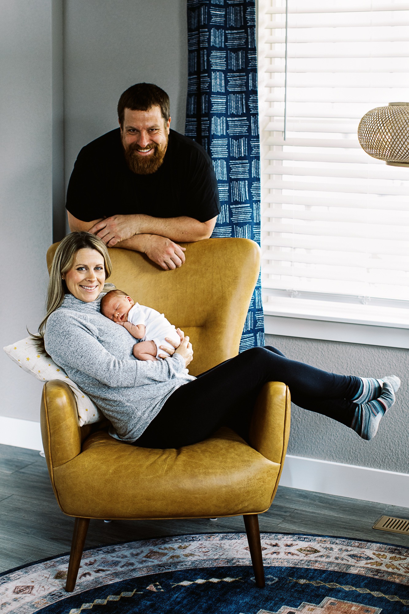 family of three including newborn babypose by leather chair