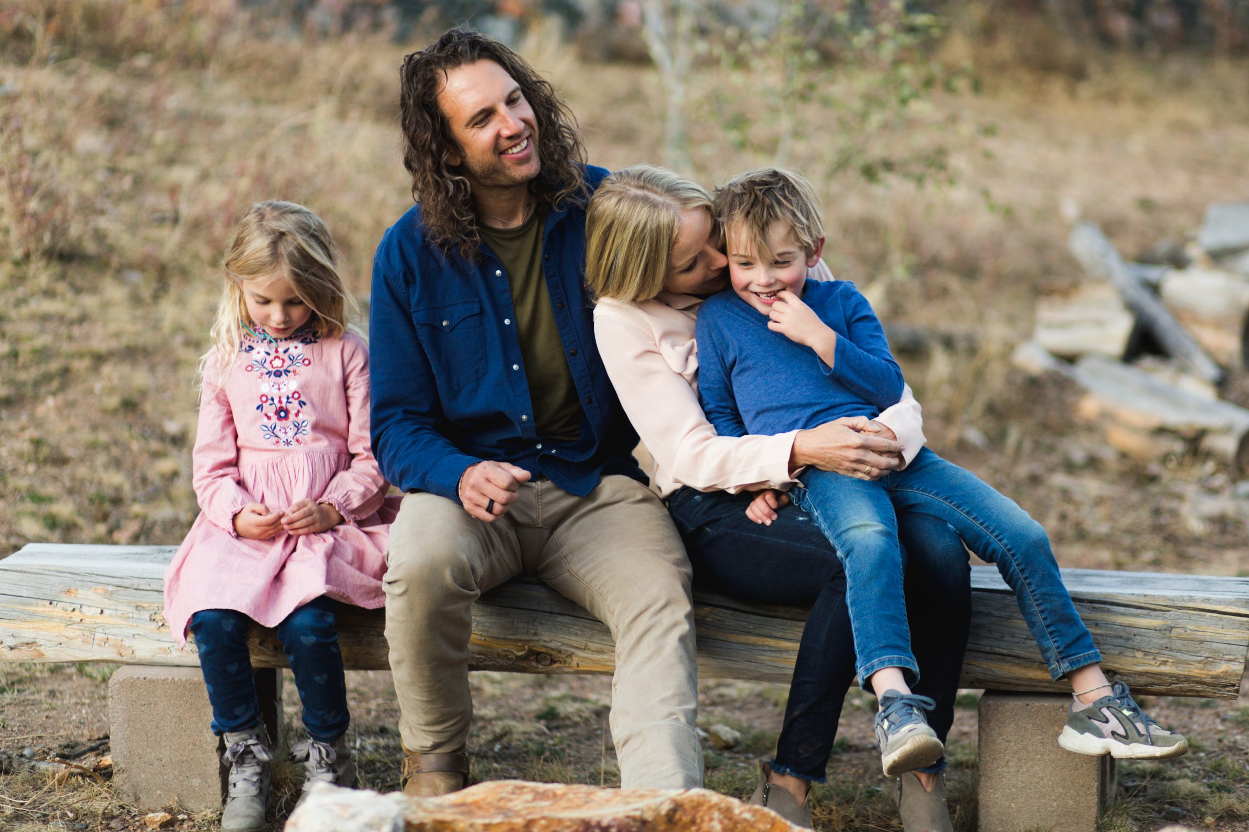 happy family sit on logs outside during a family session