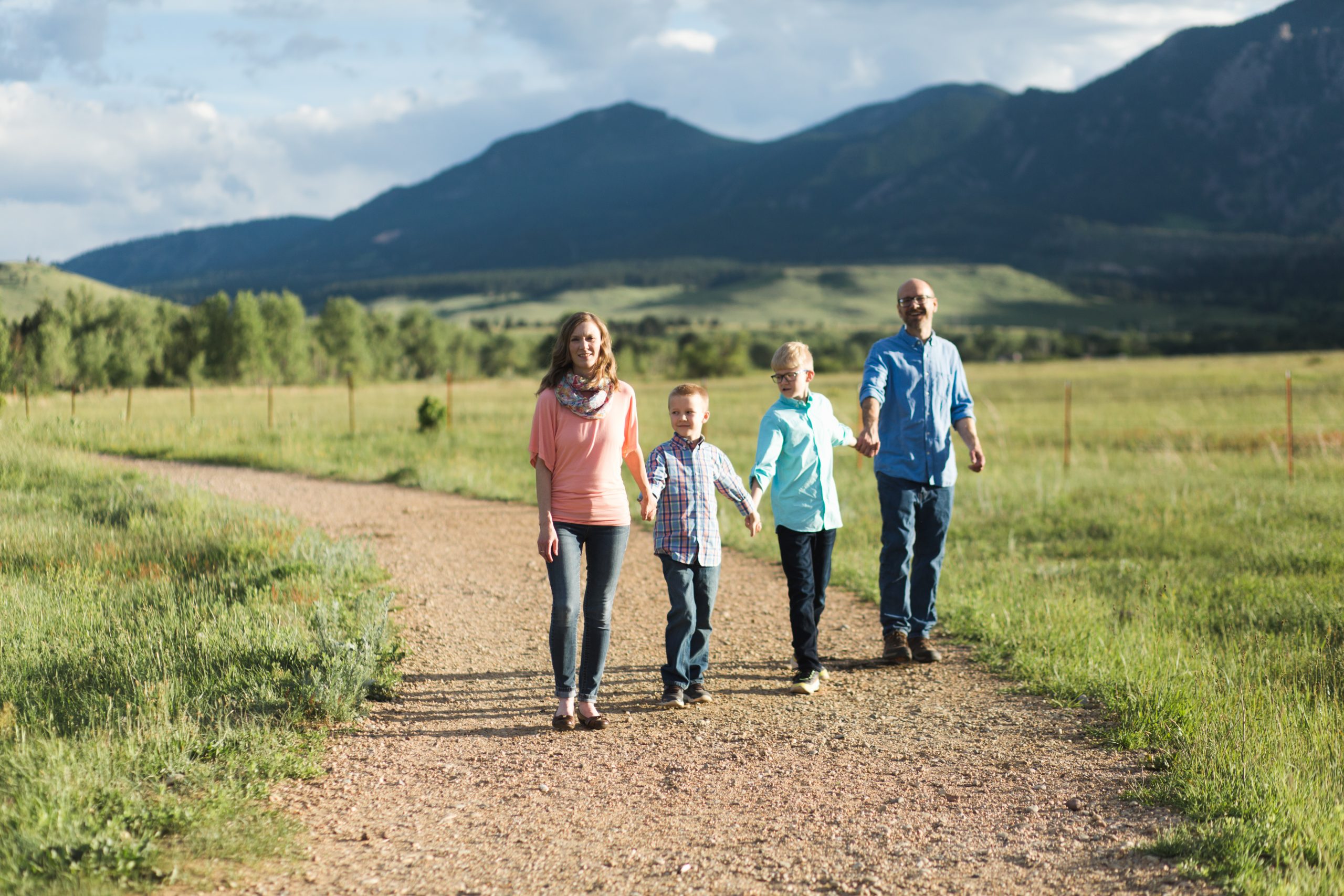 family of four hold hands and walk on a trail in front of mountains