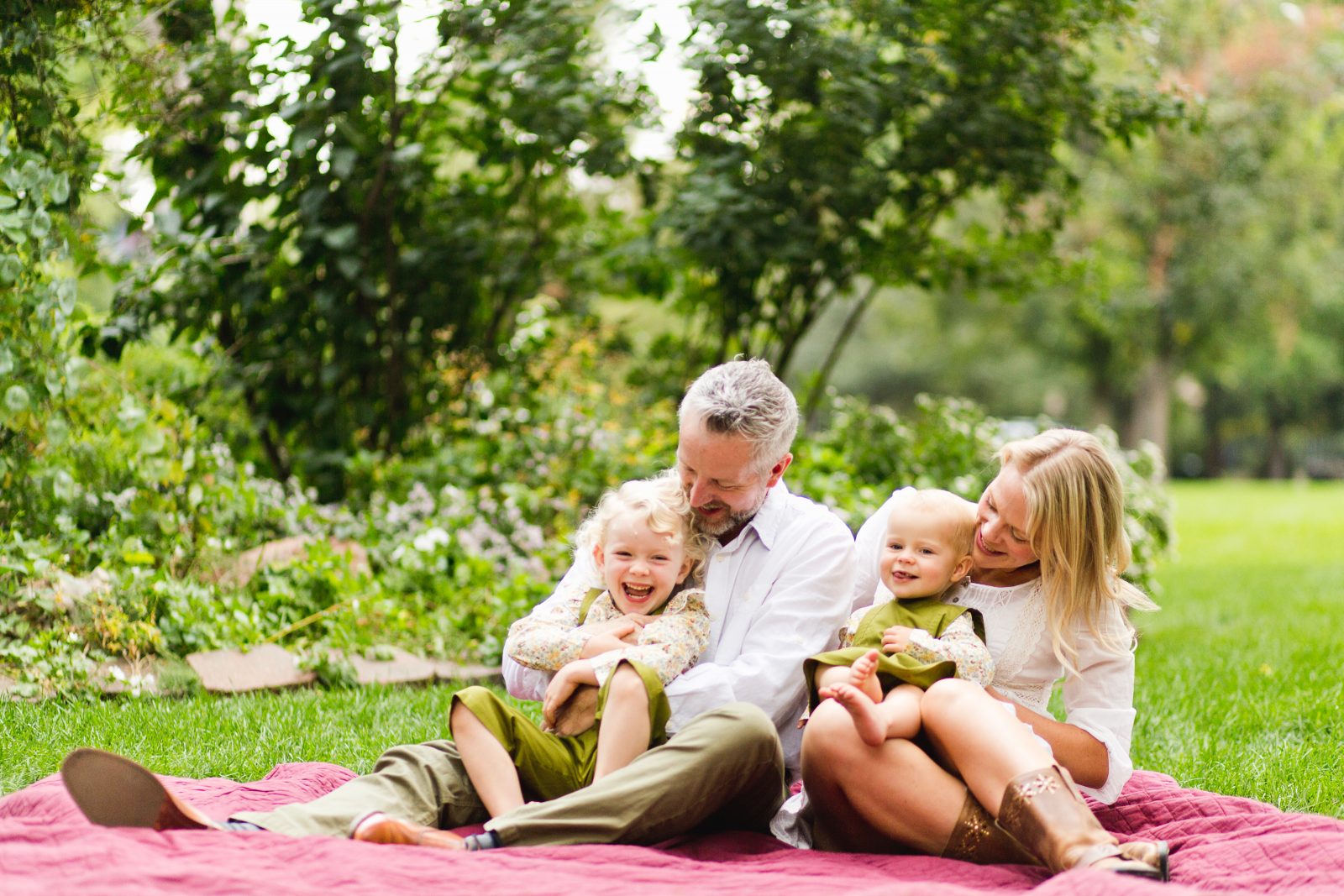 family of four sit on a blanket at a green park