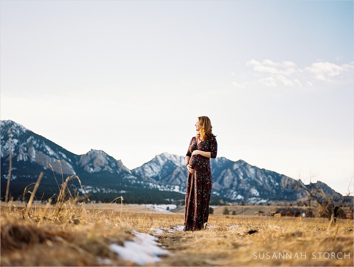 pregnant woman holds belly and looks towards mountains