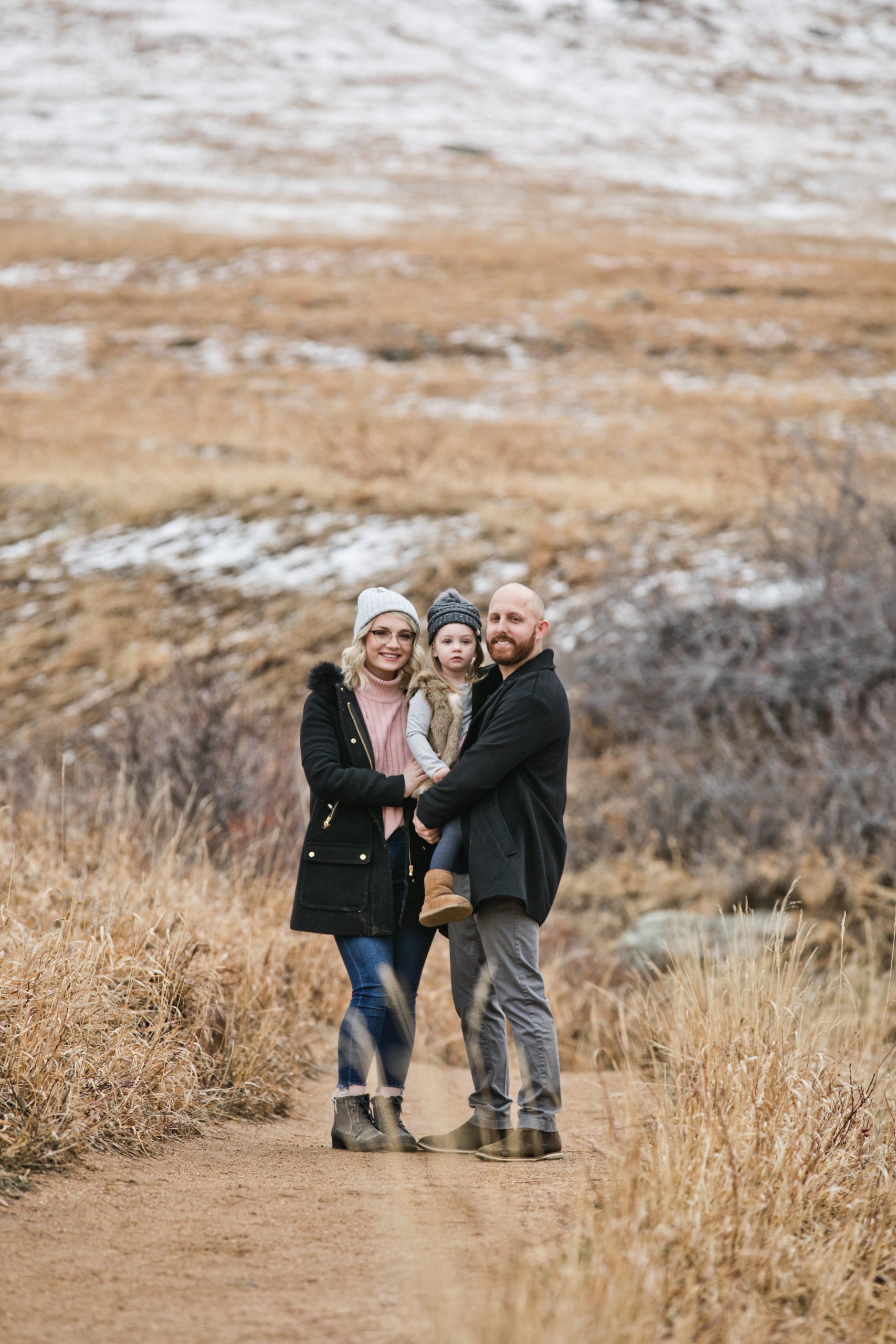 Family of three snuggle in for a photo during a winter family photo session at a park
