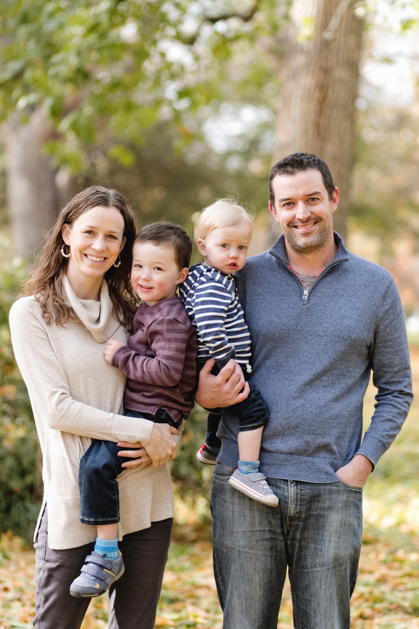 family of four stands in front of tree for fall photo session