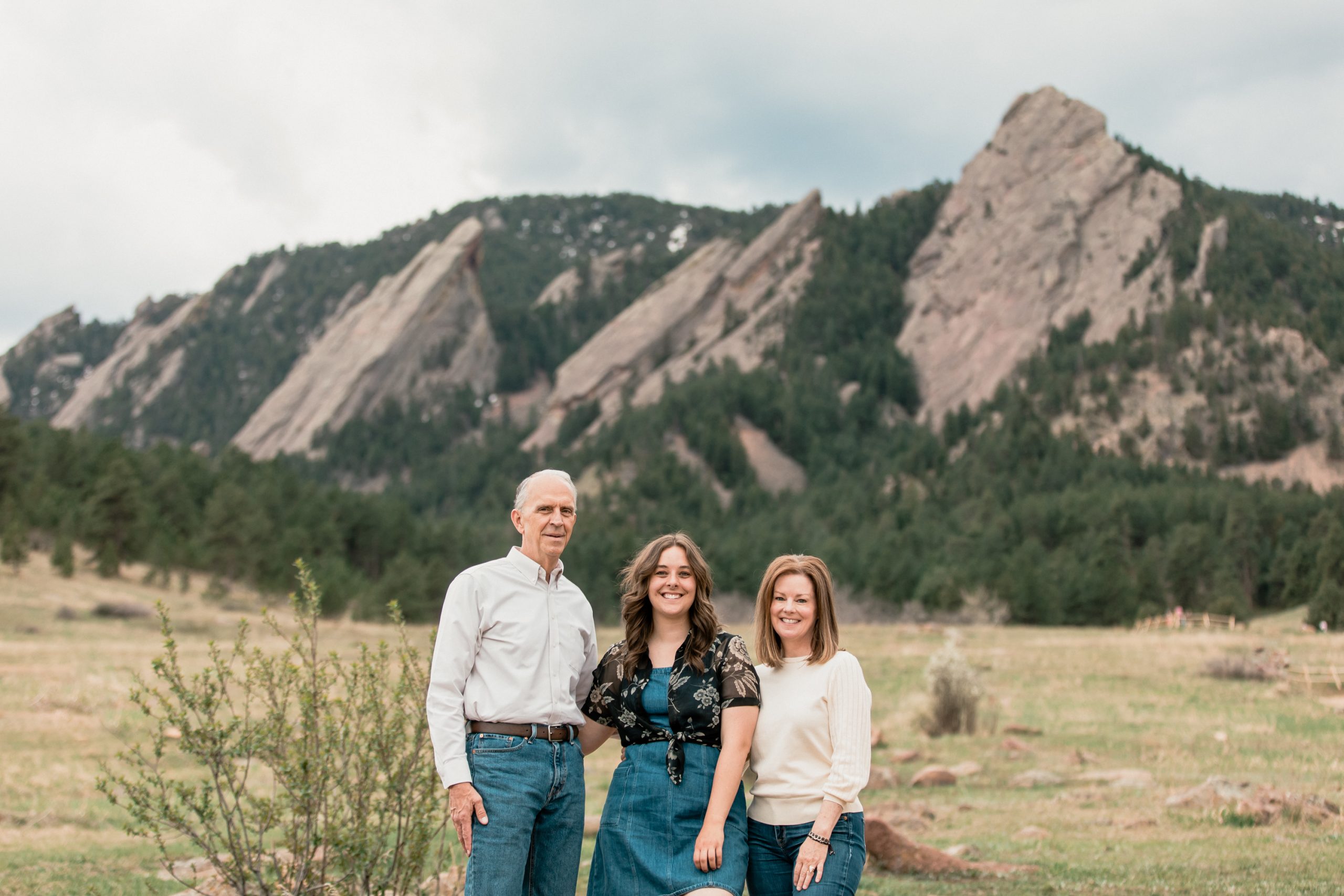 parents and their adult daughter stand in front of boulder's flatirons