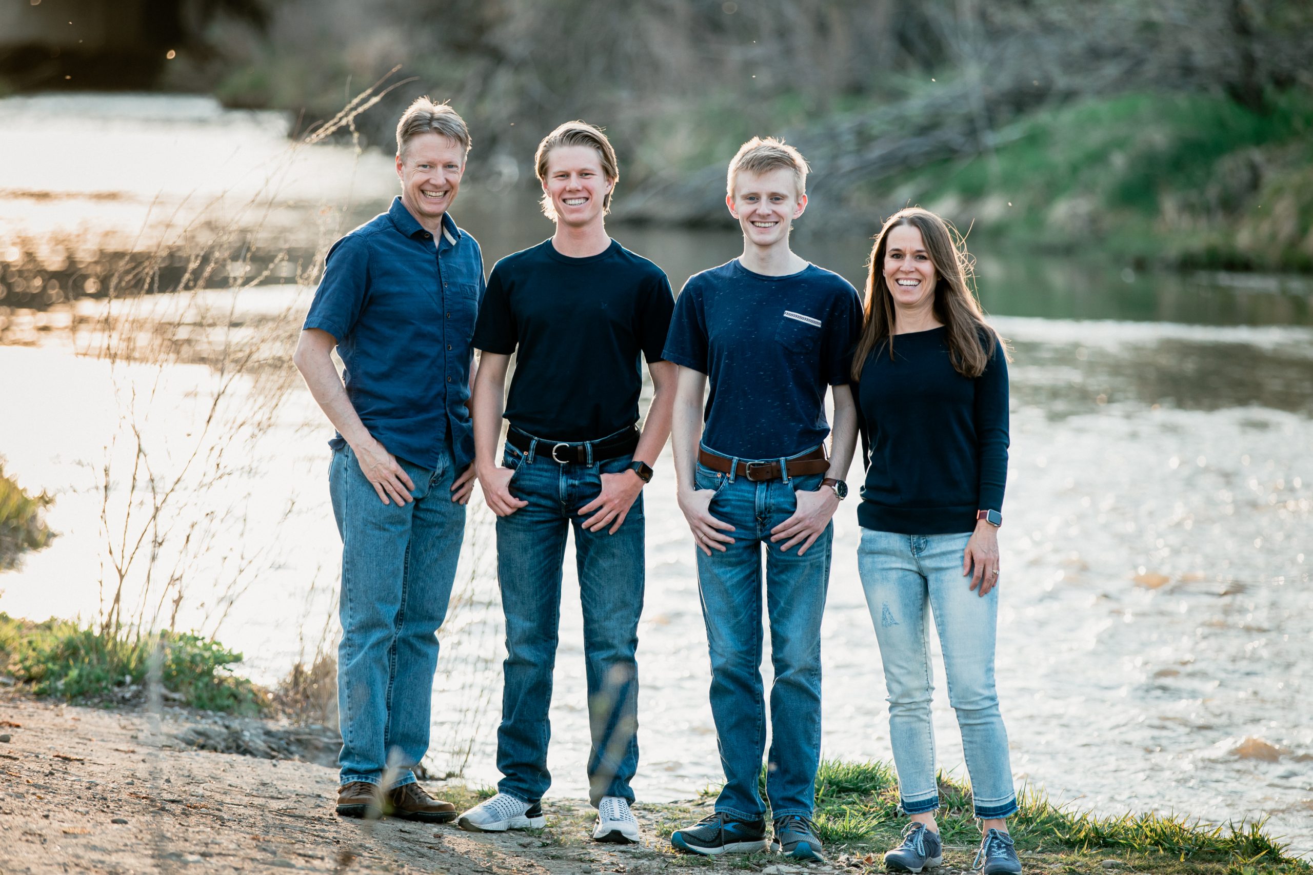 laughing longmont family with teen boys standing by river