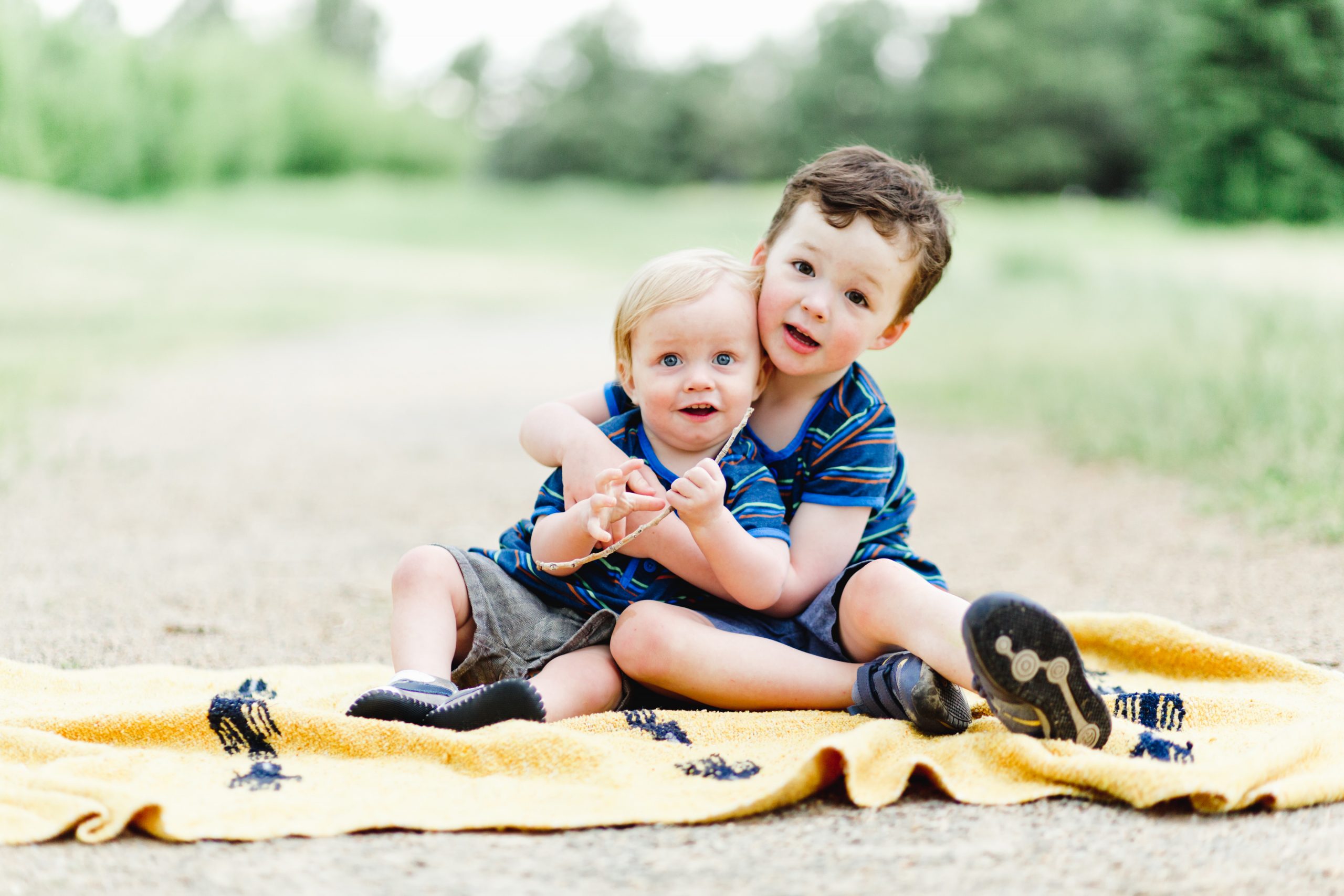 young brothers hug while sitting on a yellow blanket