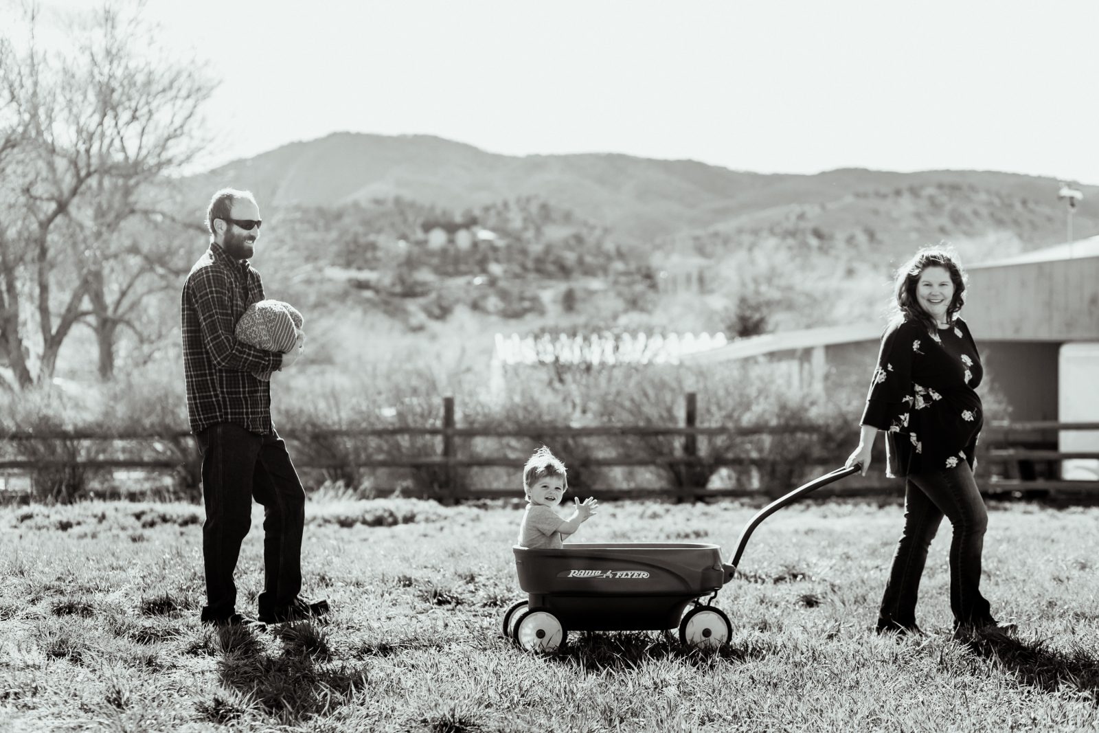 black and white photo of a mom pulling a boy in a wagon with dad and baby following behind