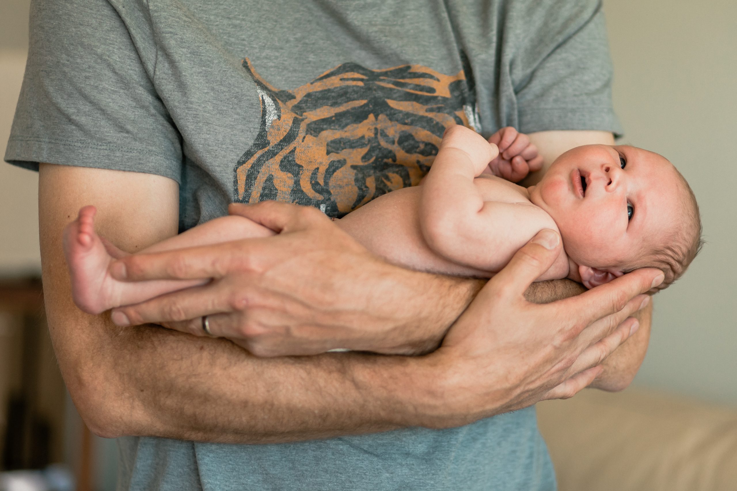 image from blog post on when to schedule a newborn photography session. photo shows a dad's arms holding his long newborn baby.