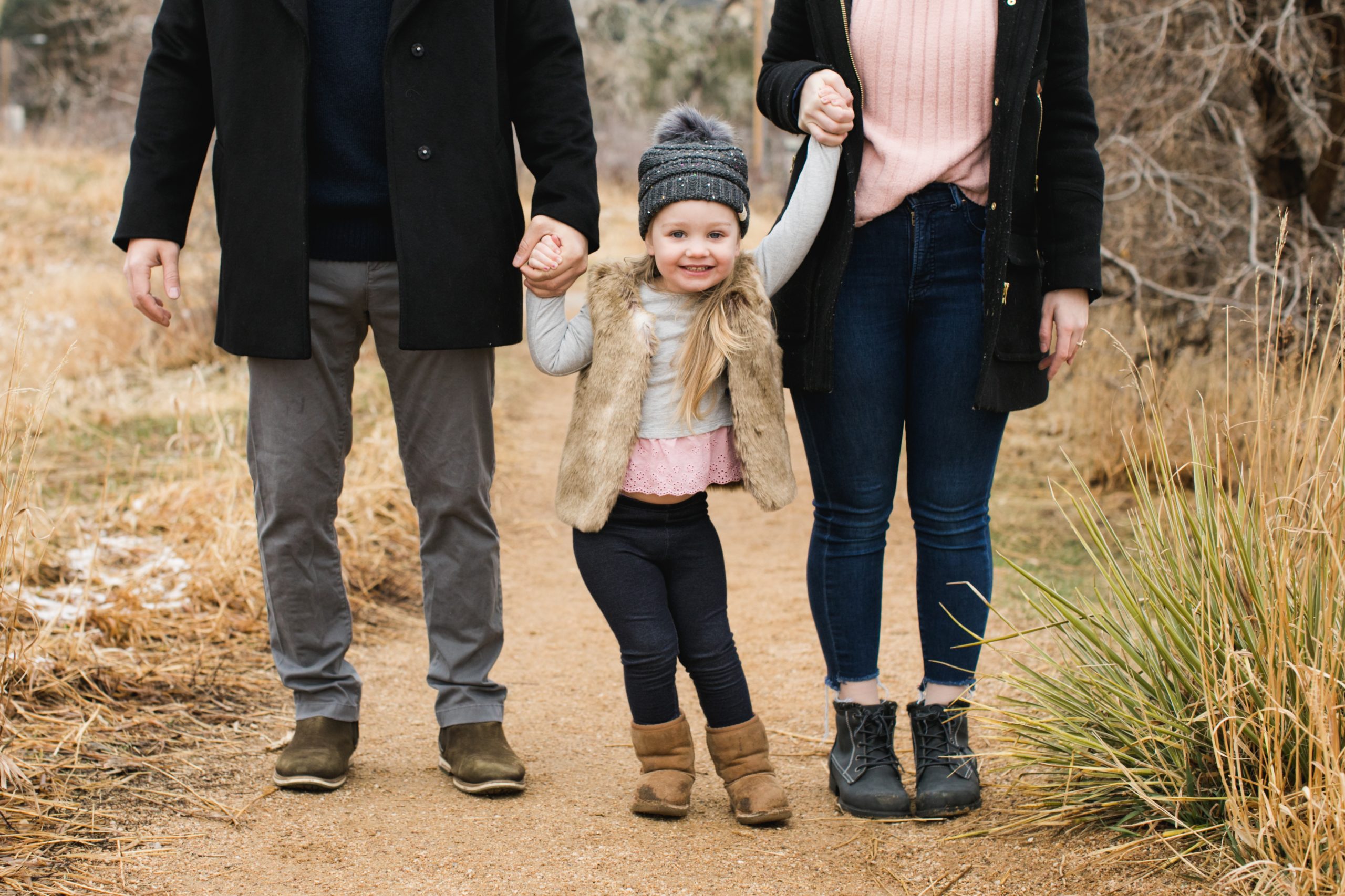 happy girl holds parent's hands during an outdoor winter photography session