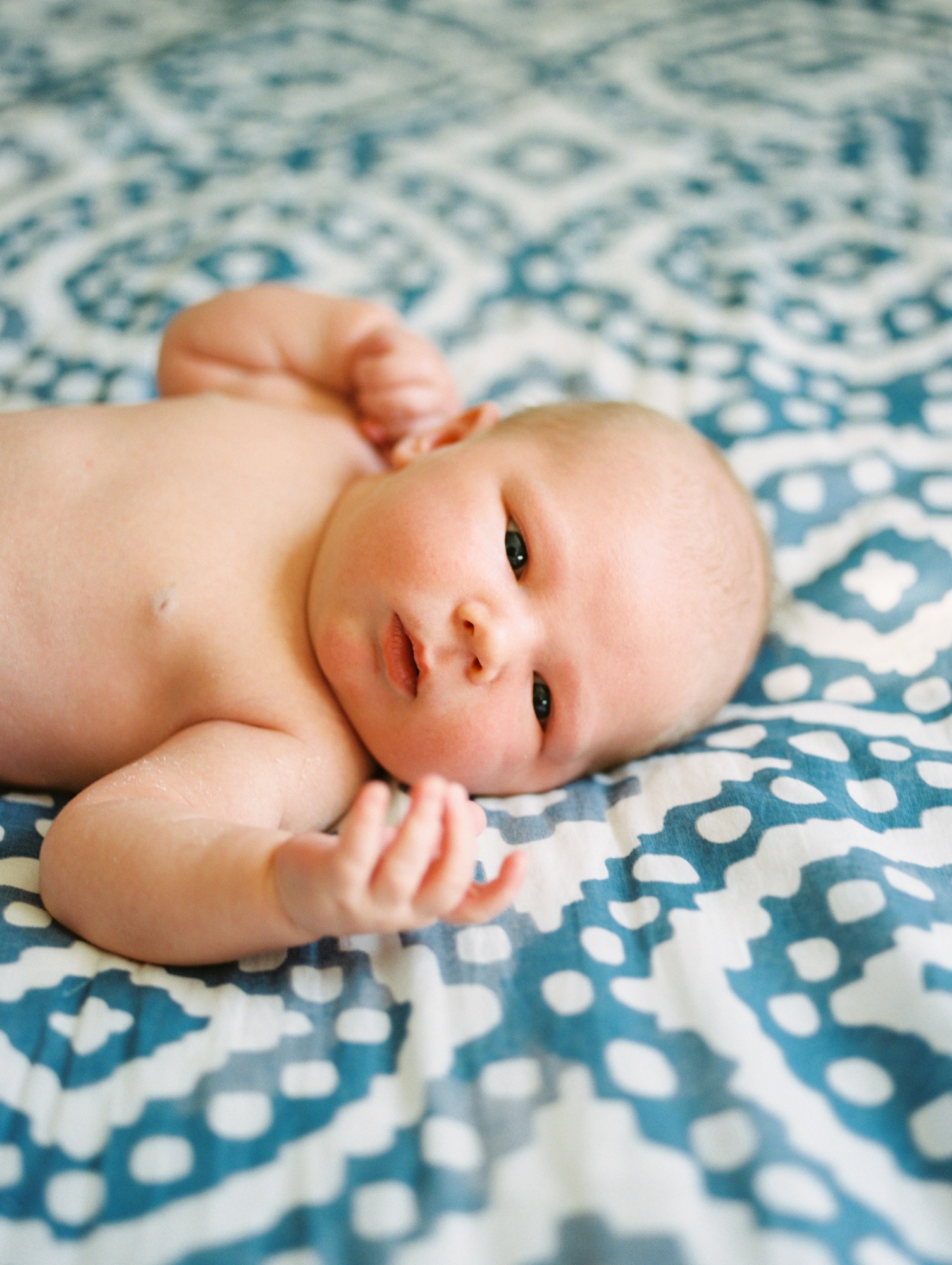 beauitful chunky baby lies on a blue and white patterned bedspread