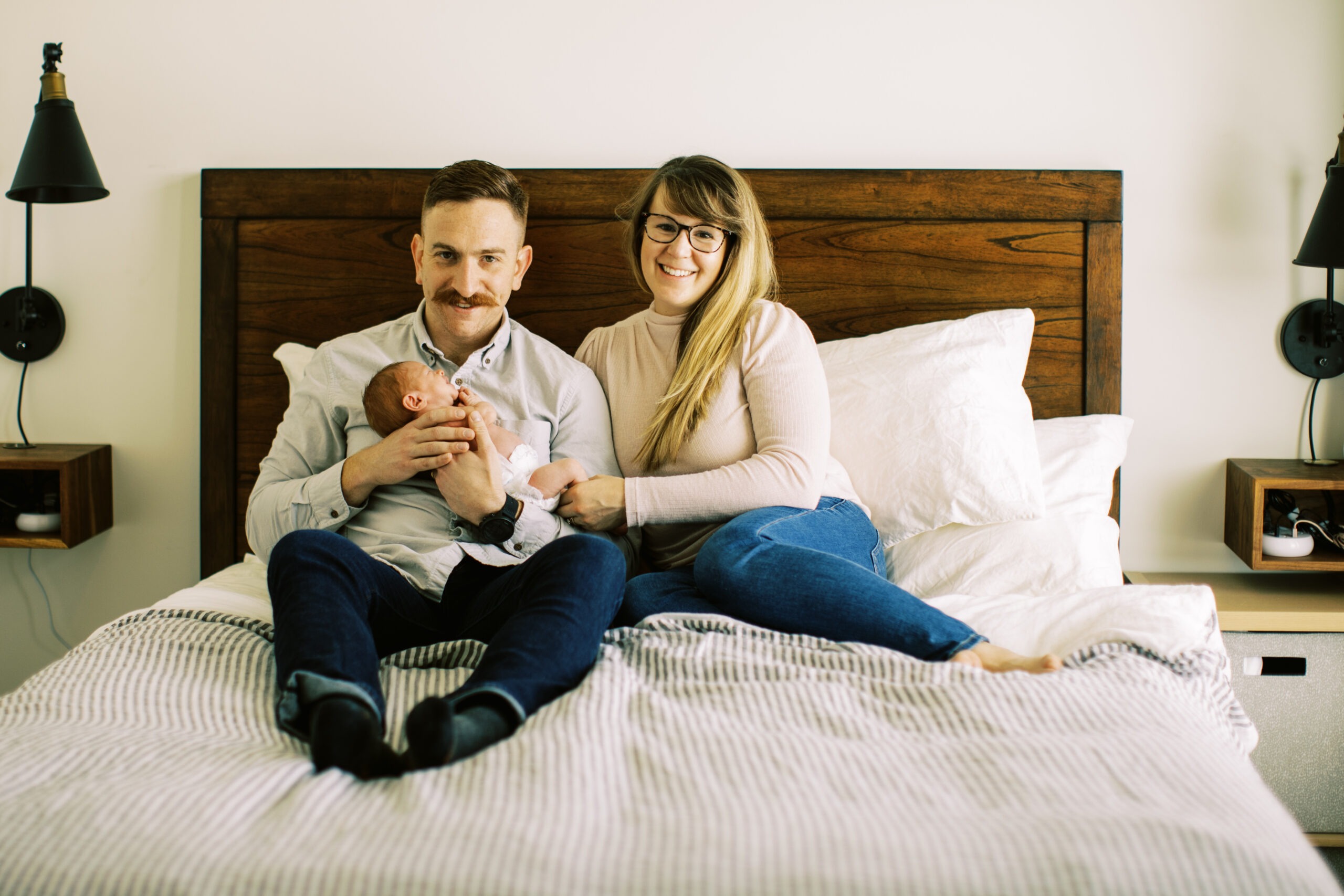 new parents sit on a bed holding their newbron baby girl
