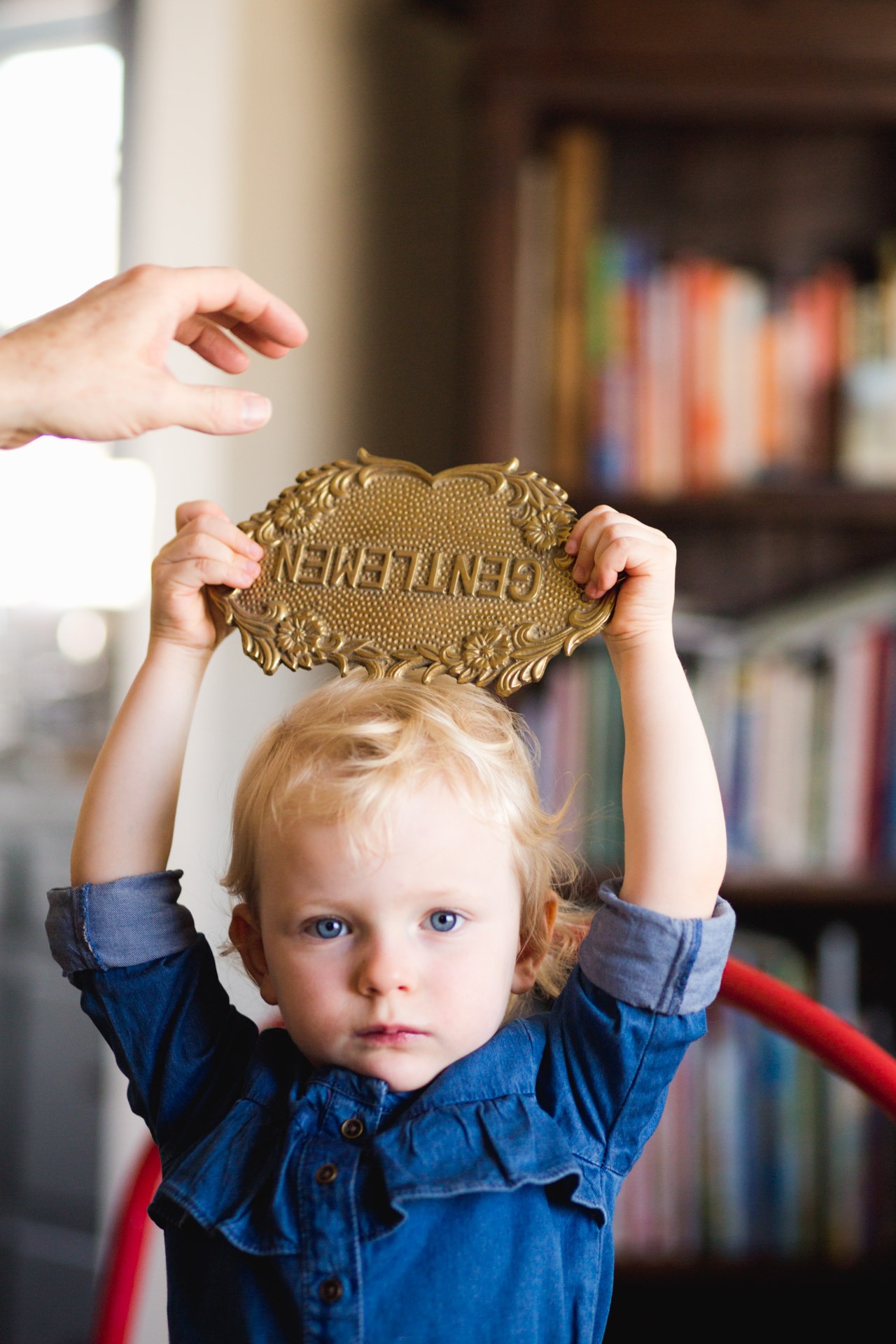 A young girl holds up a metal sign during a photo session at her home