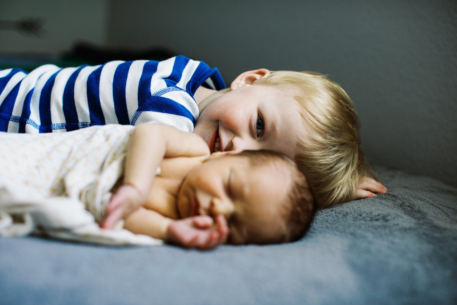 blonde brother smiles at camera behind sleeping baby brother