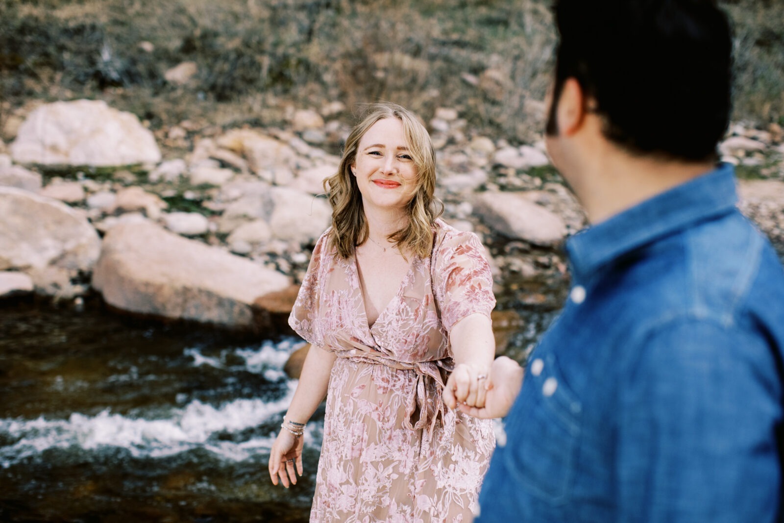 a pregnant woman smiles at camera while holding her husband's hand