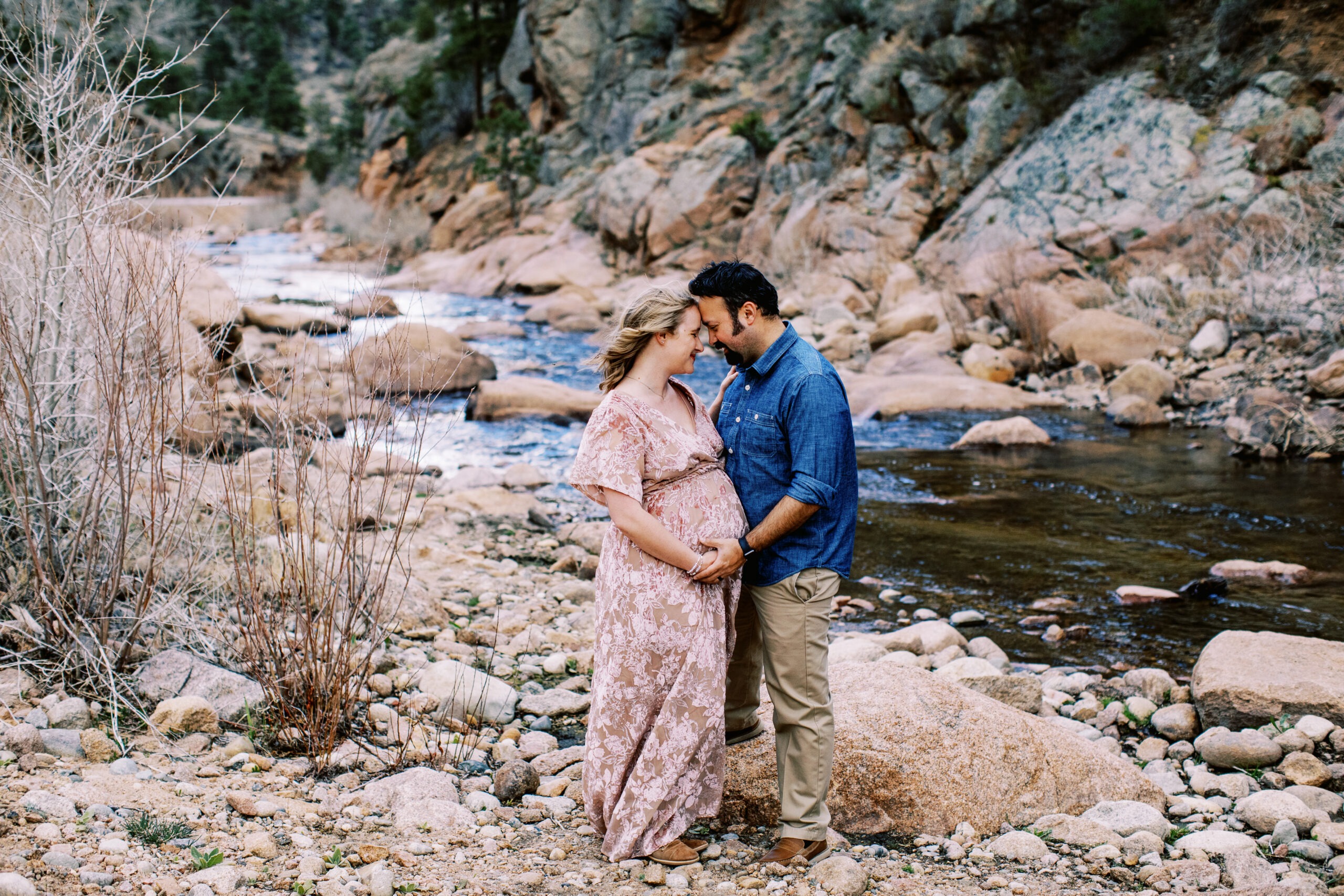 husband and pregnant wife touch foreheads by river in colorado