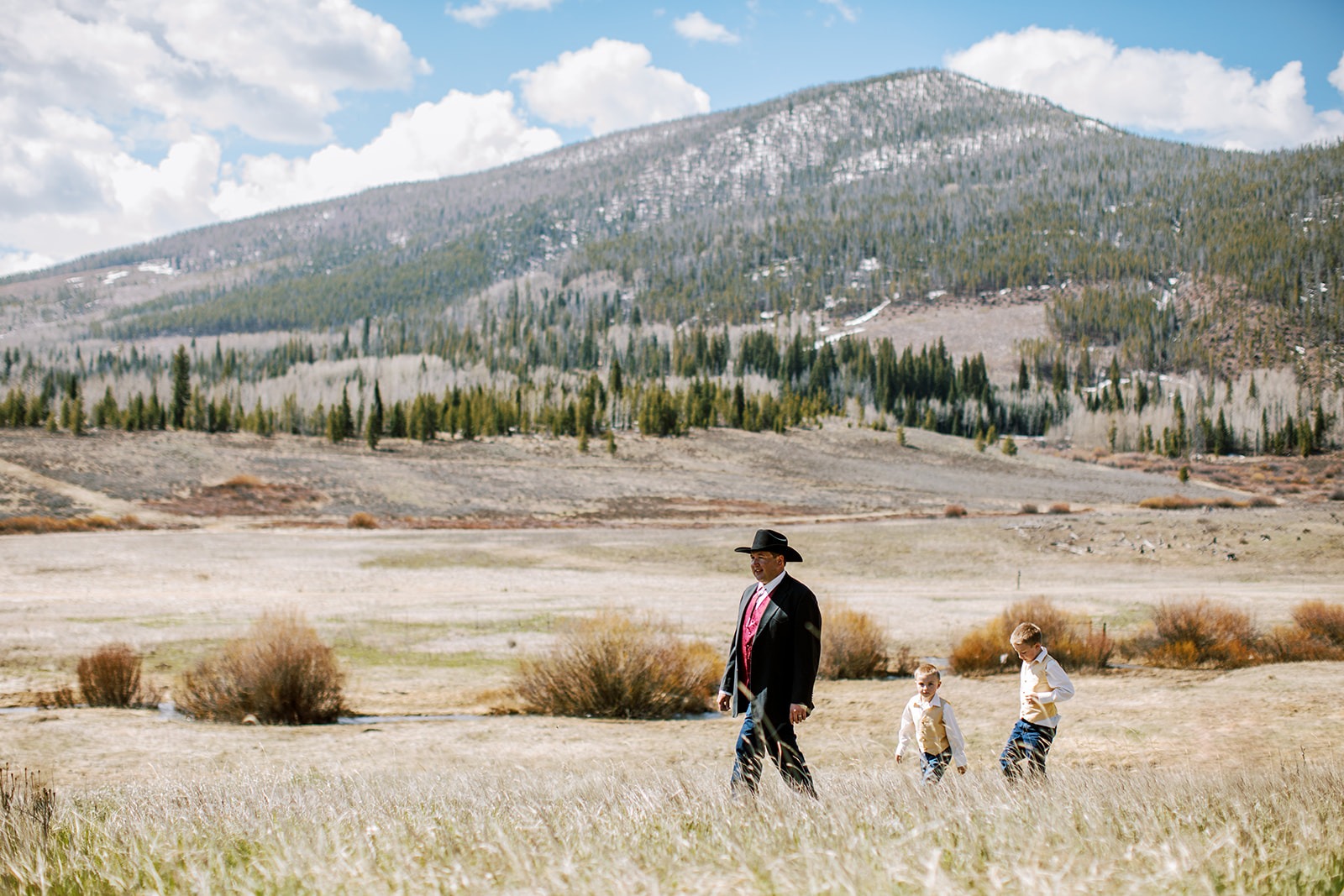 dad walks in mountain meadow with sons following him