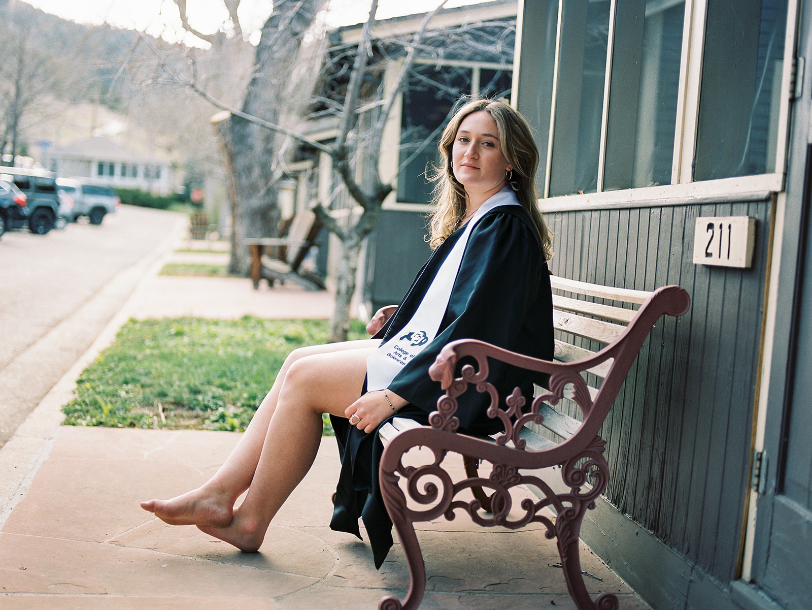 graduating woman sits on bench in front of a cabin