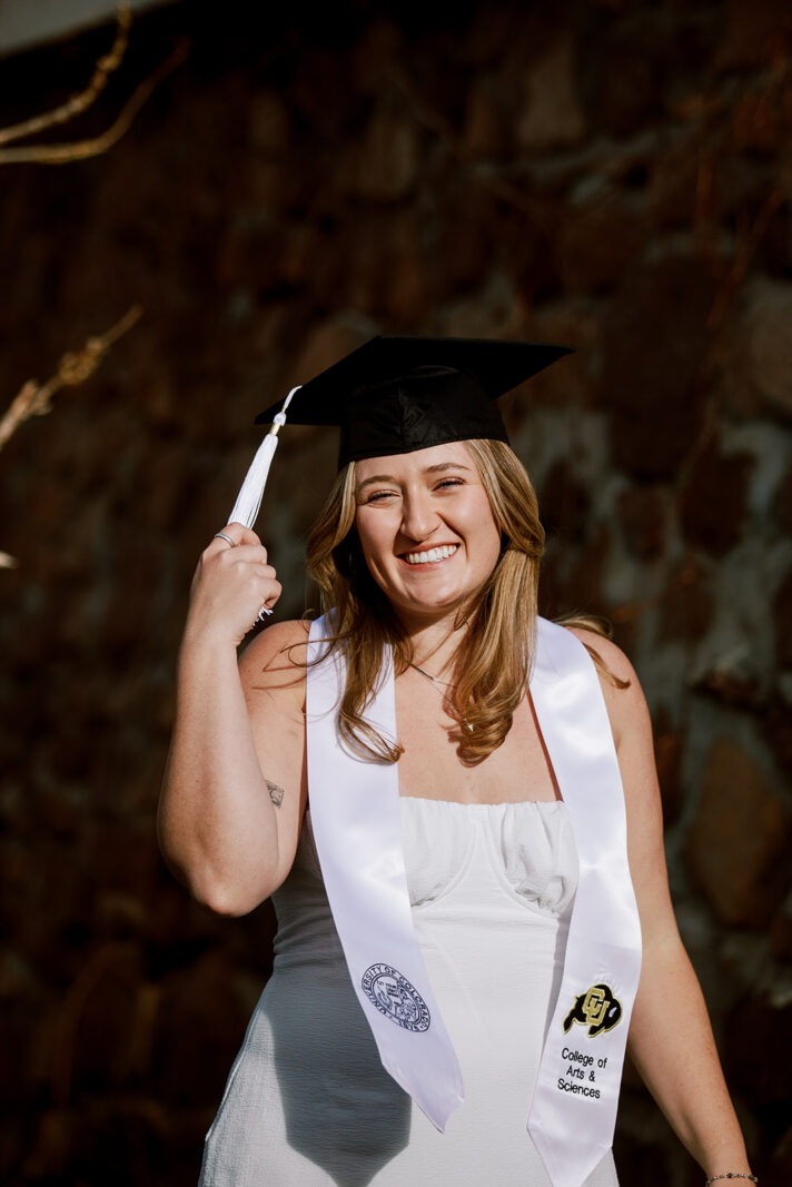 Woman smiles while wear graduation cap during graduation photoshoot